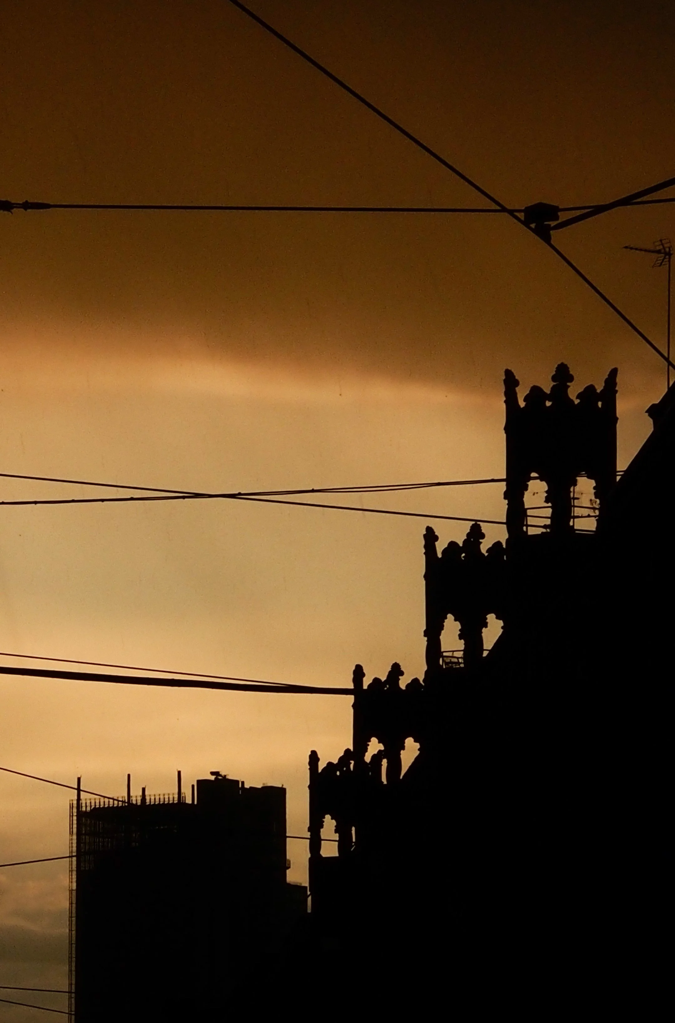 Silhouette of a historic building with ornate architectural details against a sunset sky with overhead tram wires.