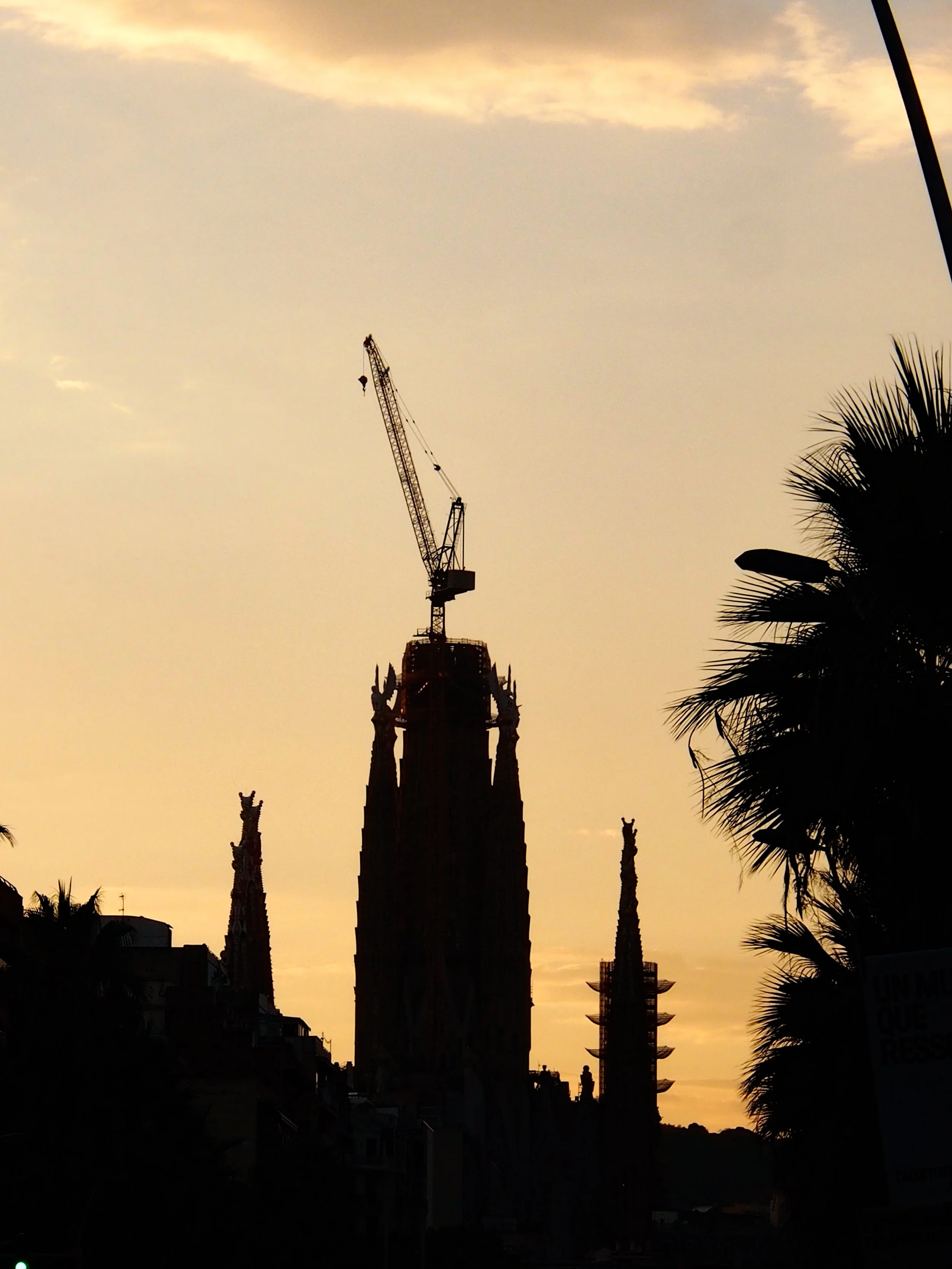 Silhouette of La Sagrada Família in Barcelona, Spain, during sunset with a construction crane on top.