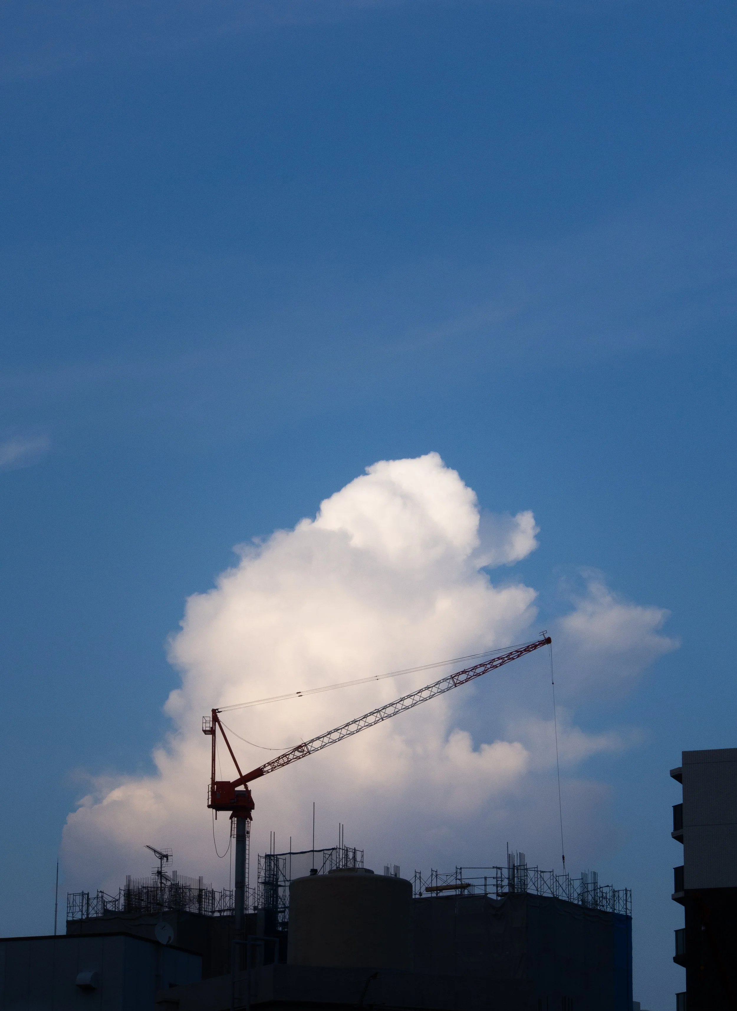 Construction crane on top of a building with cloudy blue sky in the background.