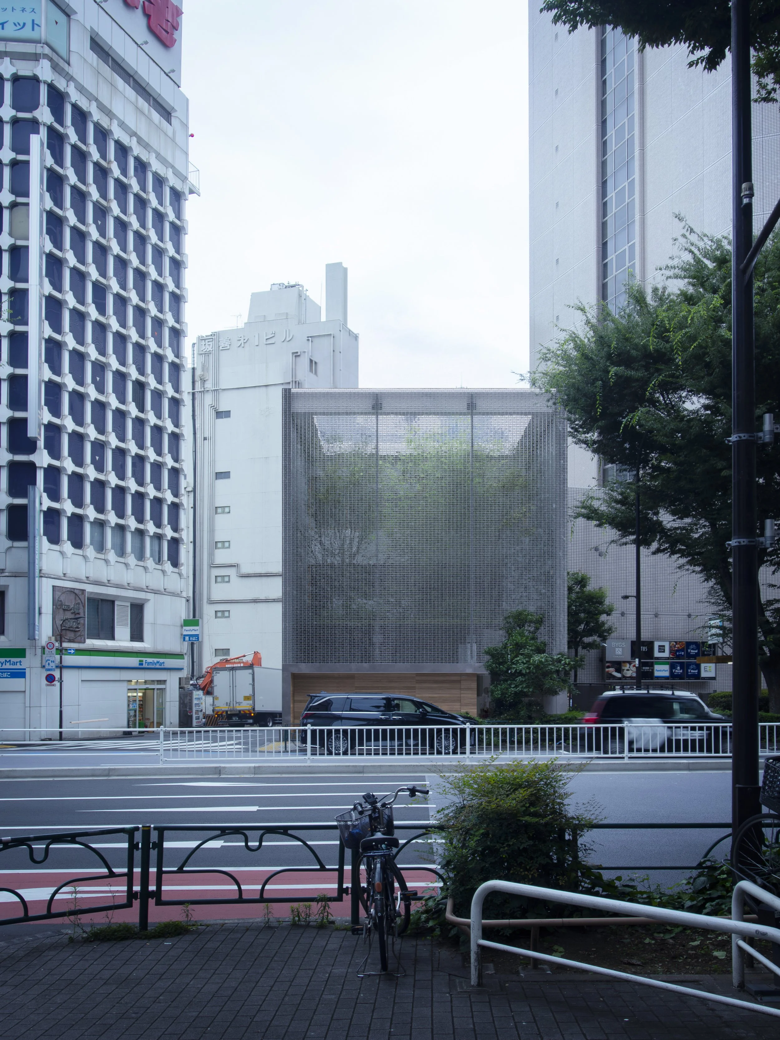 View of a city street scene with buildings, cars, a bicycle, and a red running track. Tall buildings with signage are visible in the background, and trees are on the right side of the image.