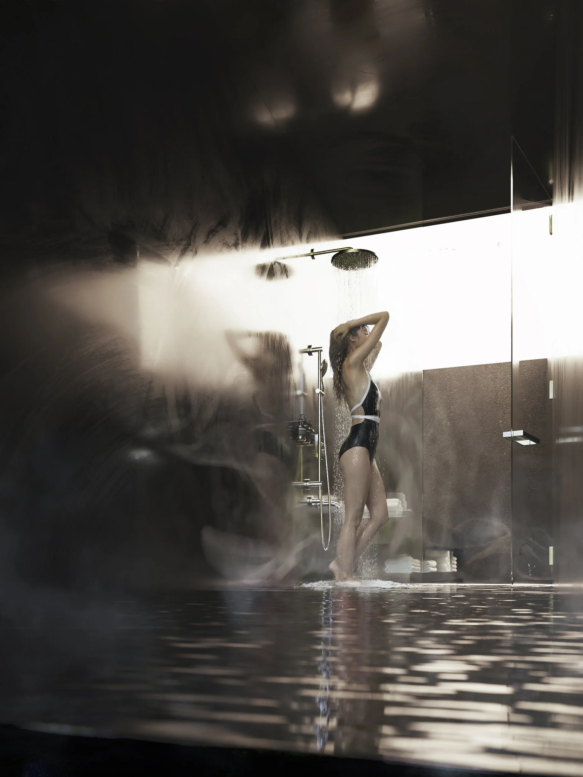 A woman taking a shower in a modern bathroom with dark walls, a rain showerhead, and a mirror reflecting her as she washes her hair.