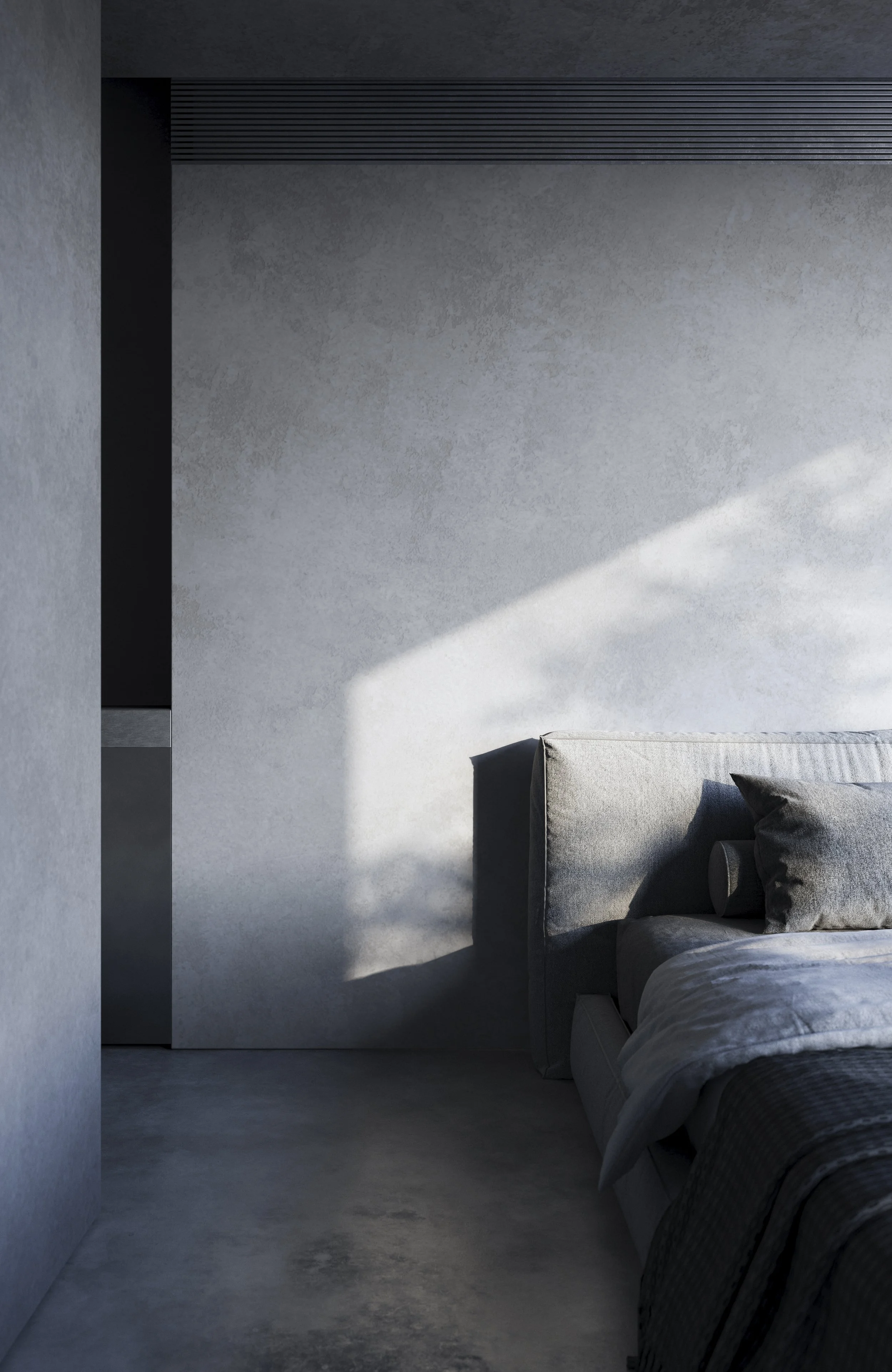 A modern bedroom with a gray upholstered bed, dark pillows, and soft lighting creating shadows on a gray wall.