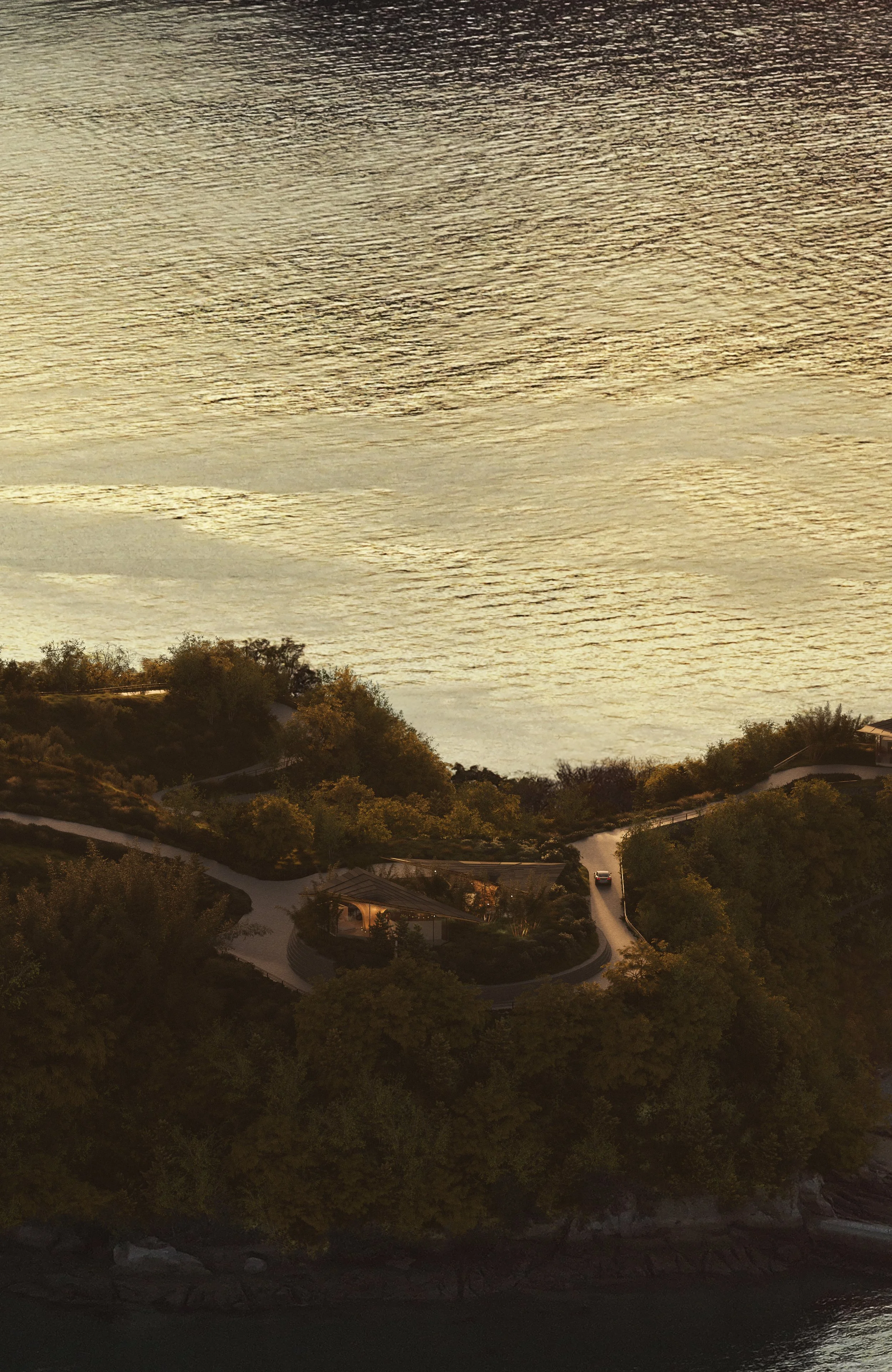 Aerial view of a winding road through lush green trees leading to a house on a hillside overlooking the ocean at sunset.