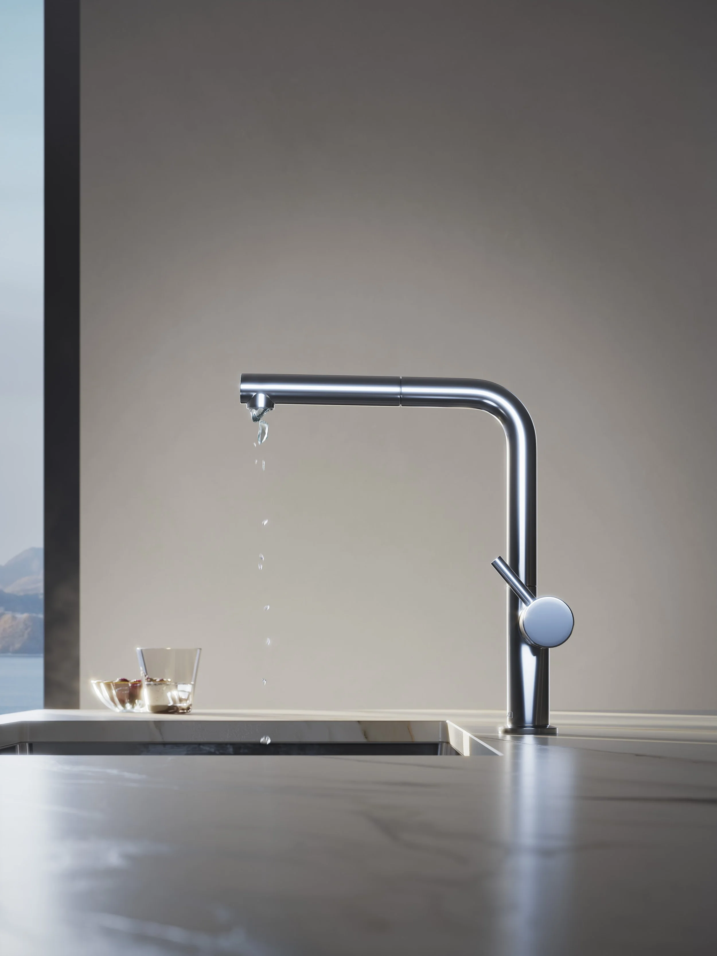 A stainless steel kitchen faucet with a glass and a bowl of fruit below it, water dripping from the spout, on a modern kitchen counter.