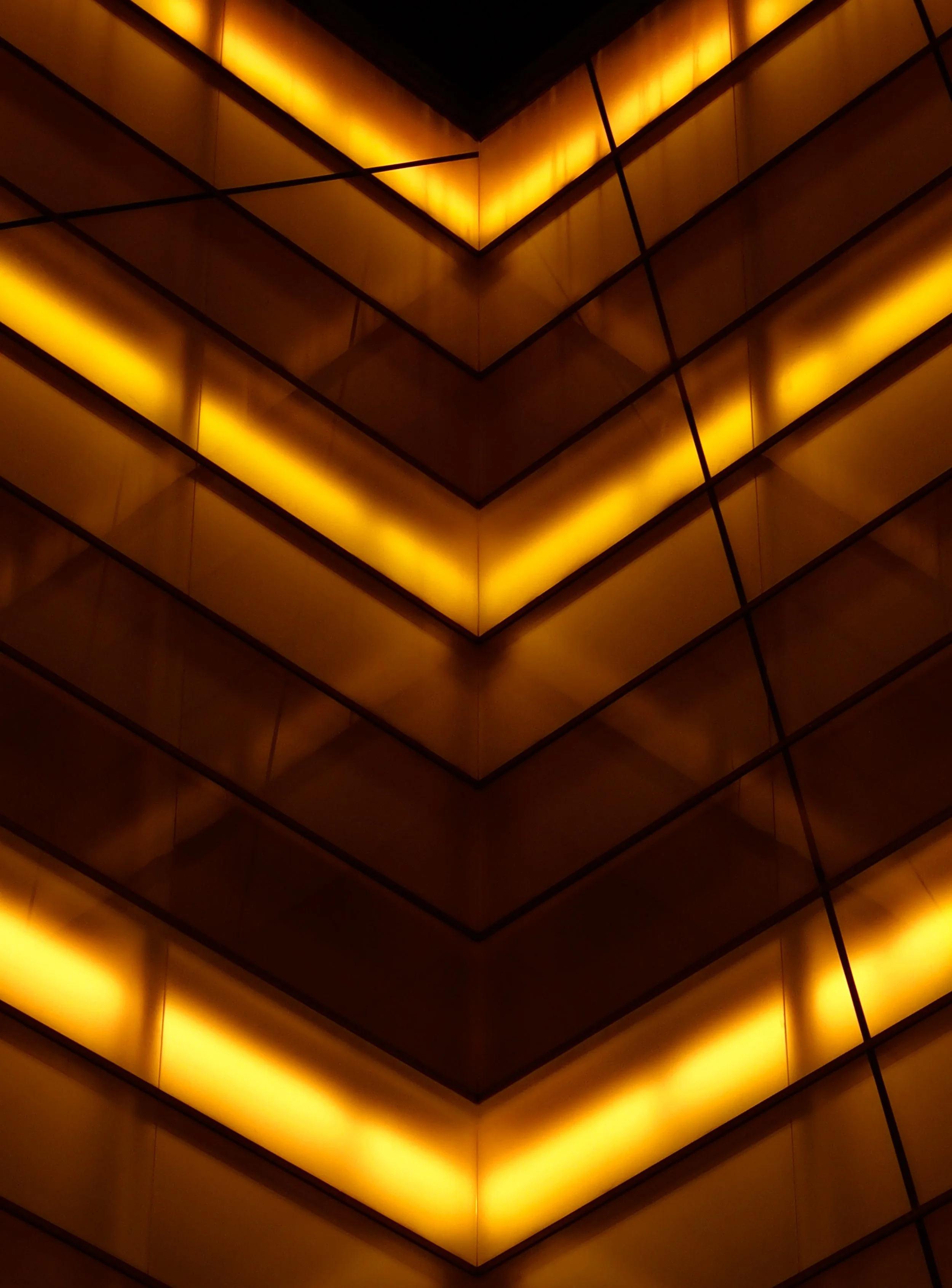 Close-up view of a modern building's exterior with illuminated yellow lighting in a geometric pattern.