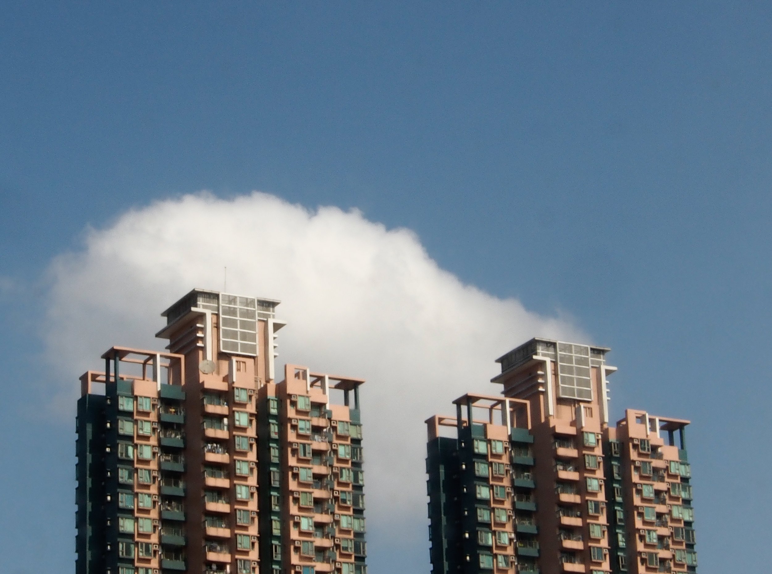 Two tall apartment buildings with many windows, topped with structures against a partly cloudy blue sky.