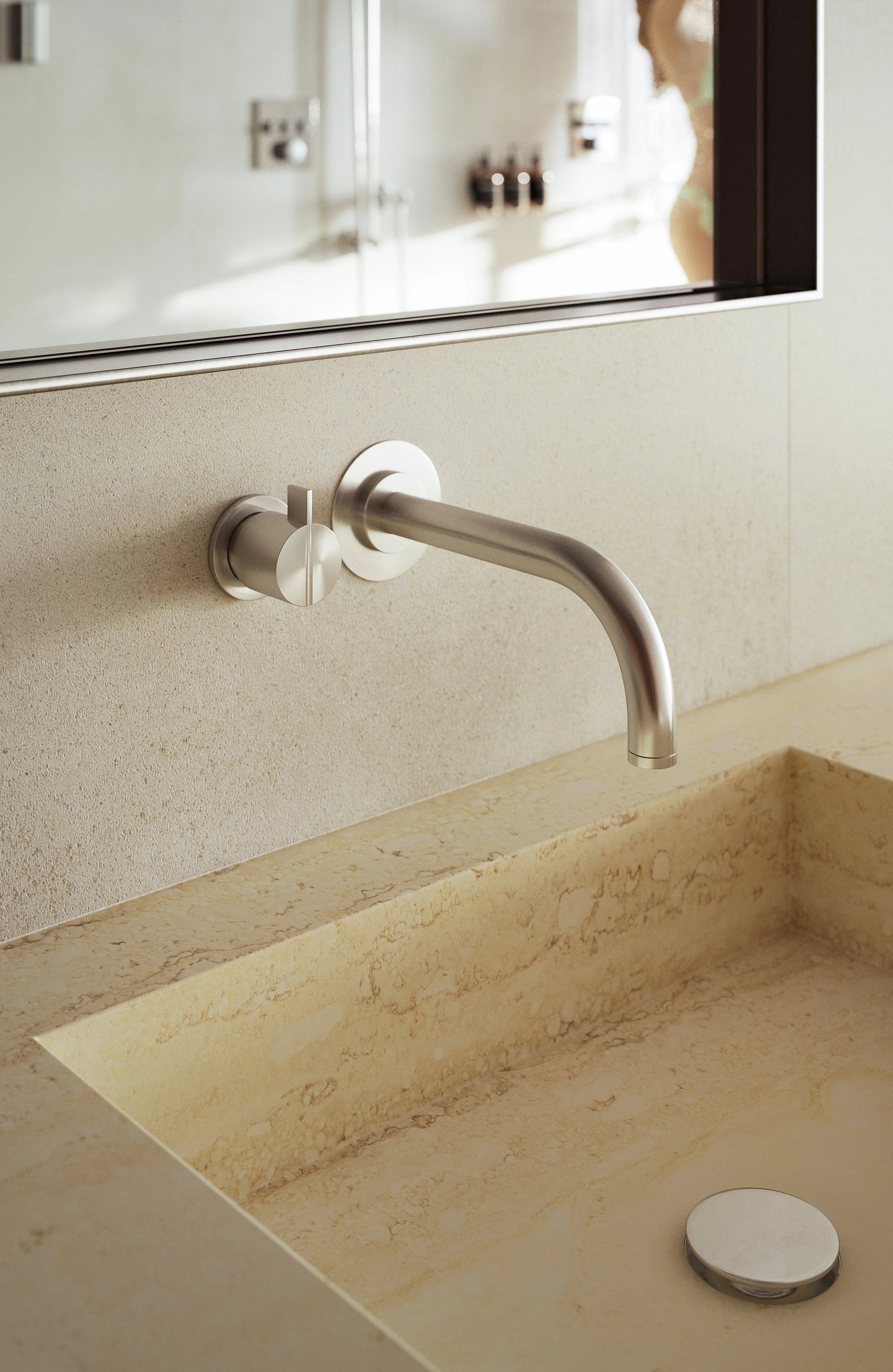 A modern bathroom sink with a beige marble countertop, a wall-mounted brushed nickel faucet, and a mirror reflecting a woman in a bathroom mirror.