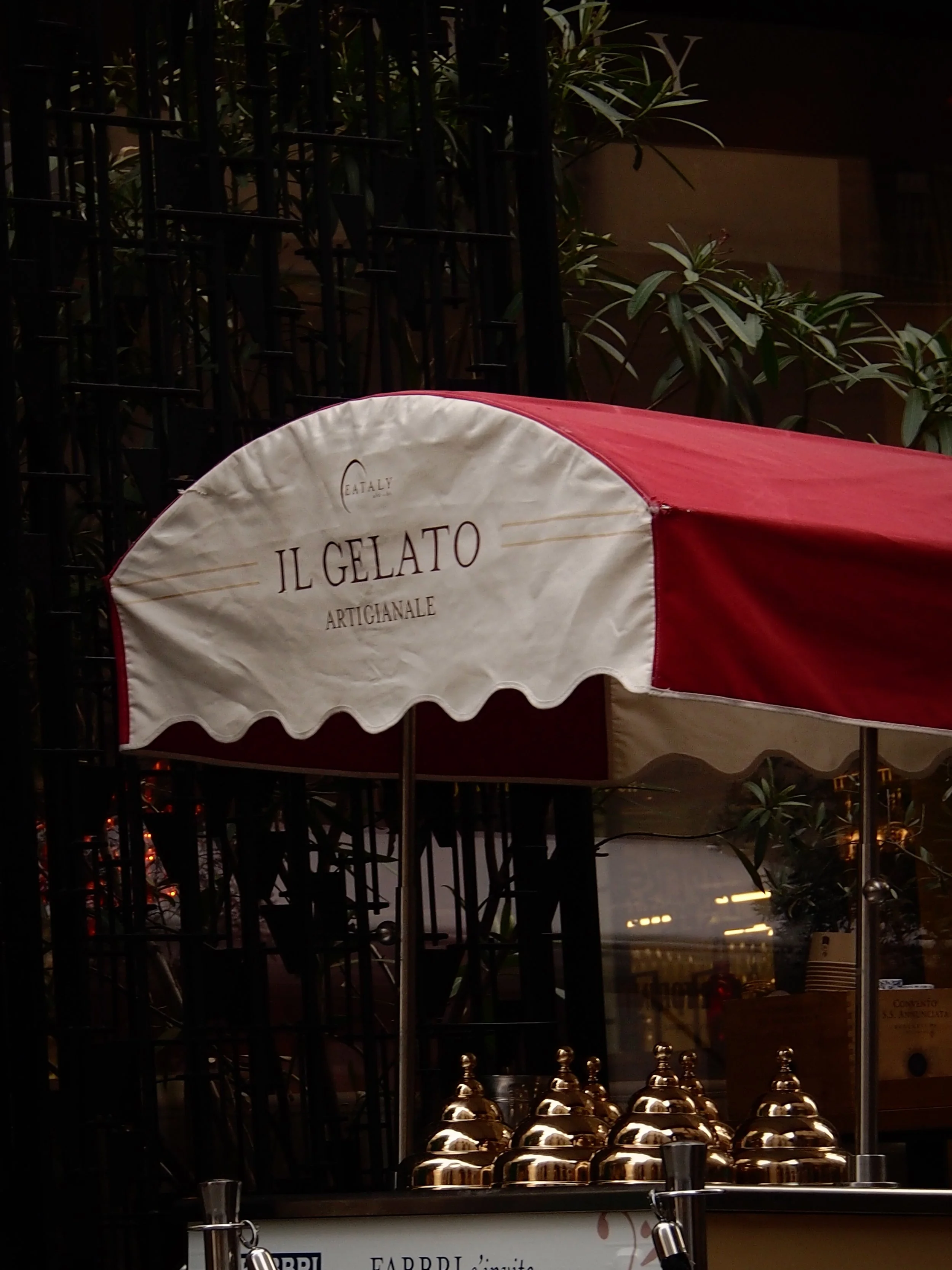 An ice cream cart with a red and white striped canopy that has the words "Il Gelato Artigianale" written on it, and a few golden-topped containers on display.