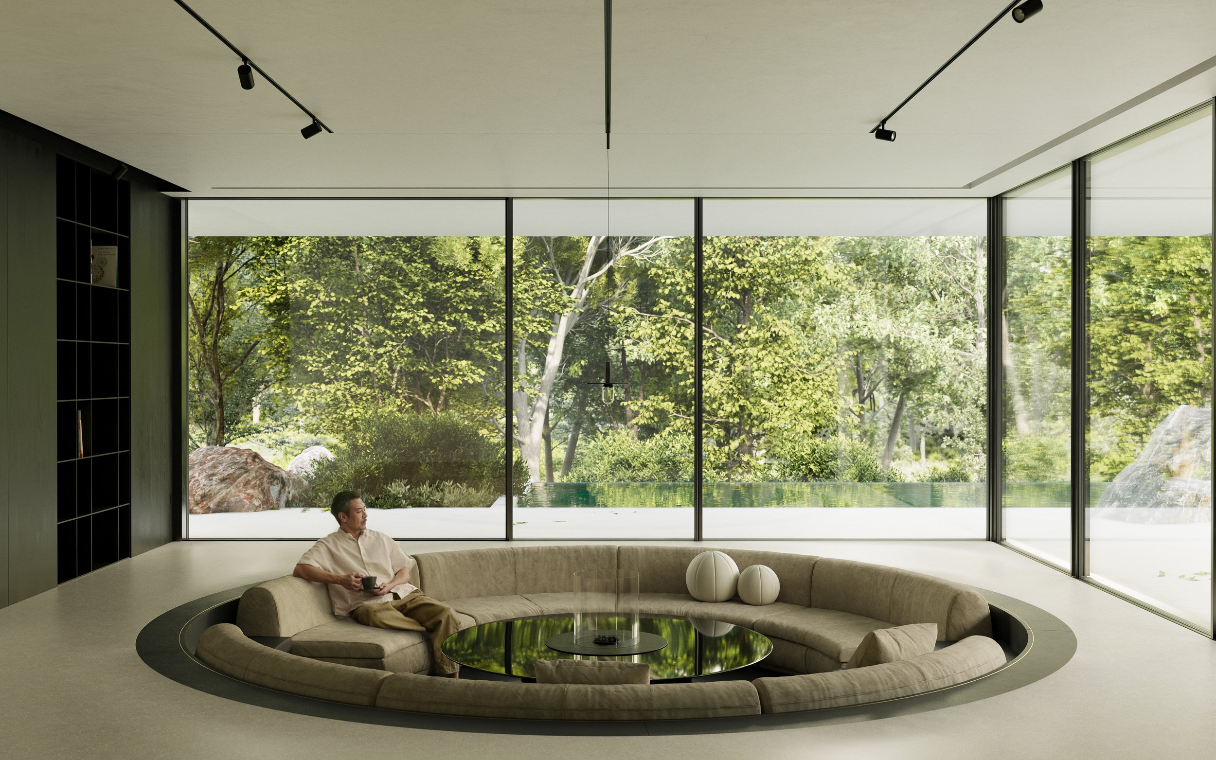 Inside a modern, minimalist living room with large floor-to-ceiling glass windows showing a lush green outdoor landscape. A man is sitting on a circular beige sofa holding a drink, with a round black coffee table in front of him. The room features a 