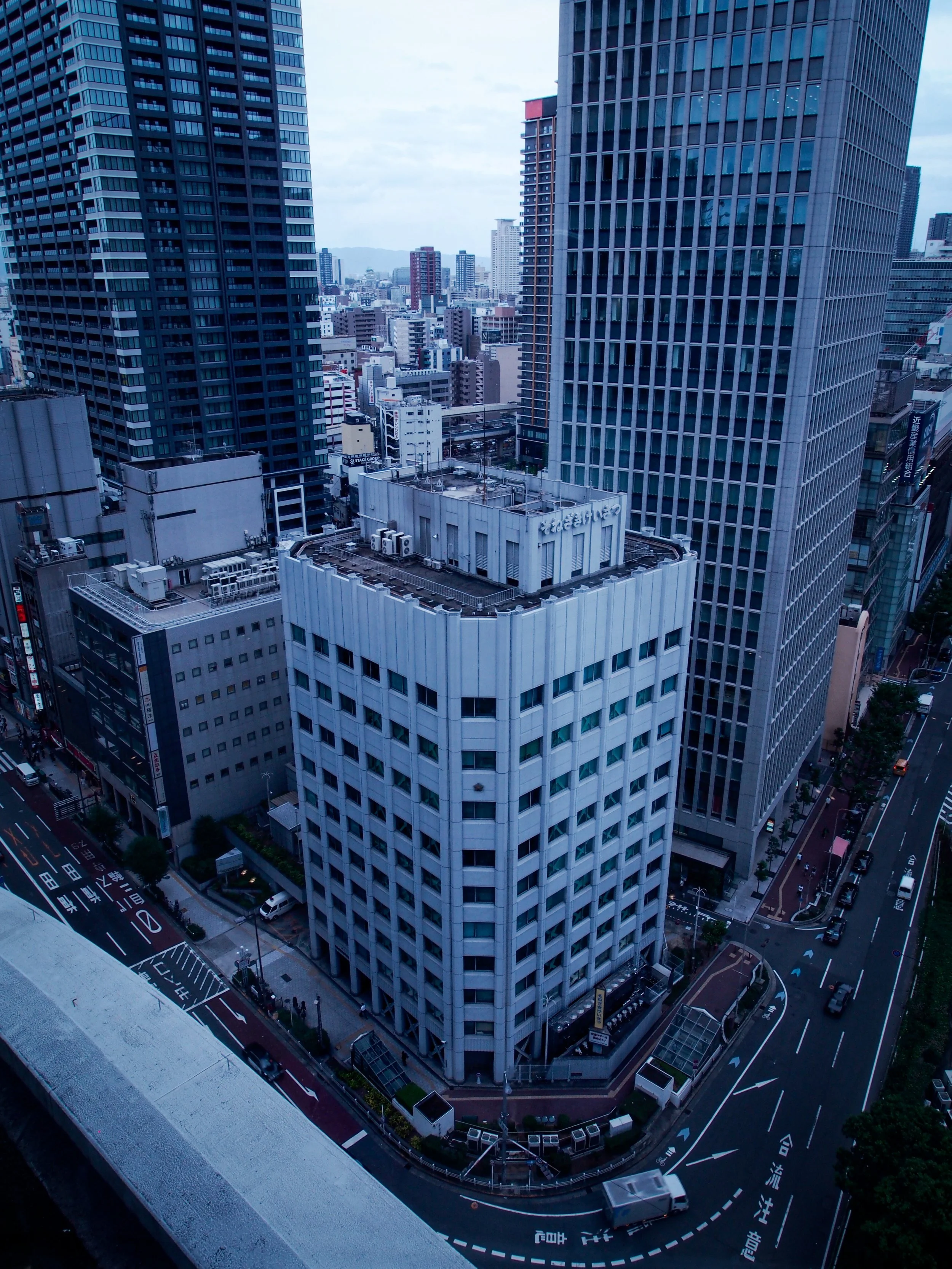 A cityscape view from a high-rise, showing multiple tall office buildings, streets, and cars in an urban area.