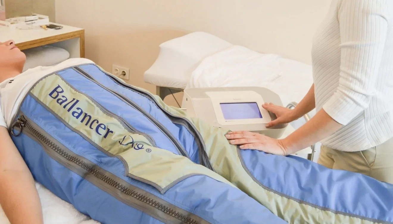 A person lying on a hospital bed covered with a blue and yellow ballistic blanket, with a healthcare worker attending to the patient and operating a medical device.