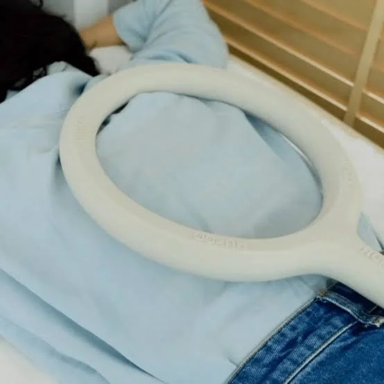 Person lying in a hospital bed with a CT scan or MRI scanner tool placed on their abdomen.