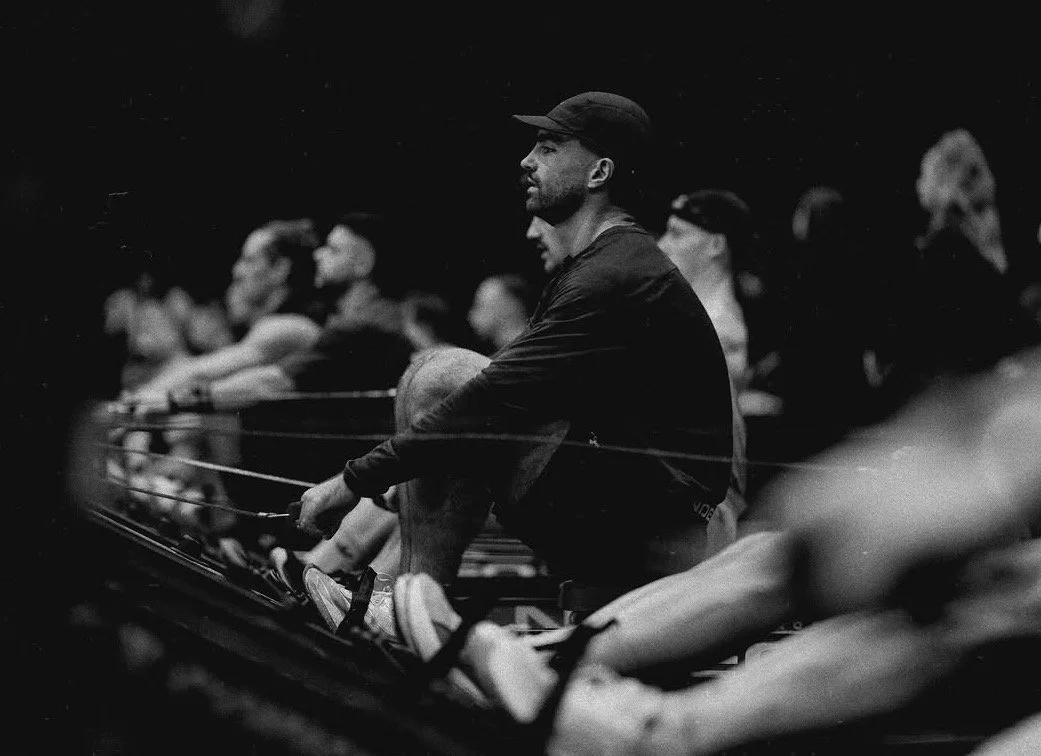 Un groupe de personnes assises dans une salle, probablement lors d'une séance d'entraînement ou de cours, avec un focus sur un homme porteur d'une casquette. L'image est en noir et blanc.