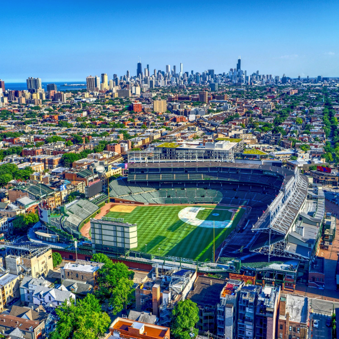 Aerial view of a baseball stadium in an urban city with high-rise buildings in the background and a clear blue sky.