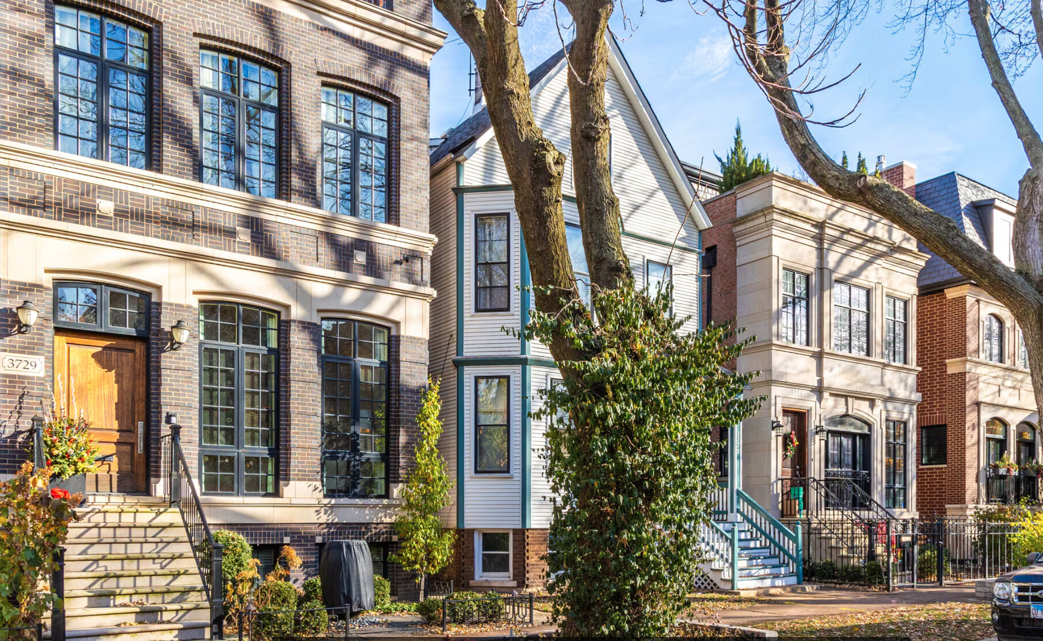 Row of urban houses with varied architectural styles, some modern with large windows, across a tree-lined street in daylight.