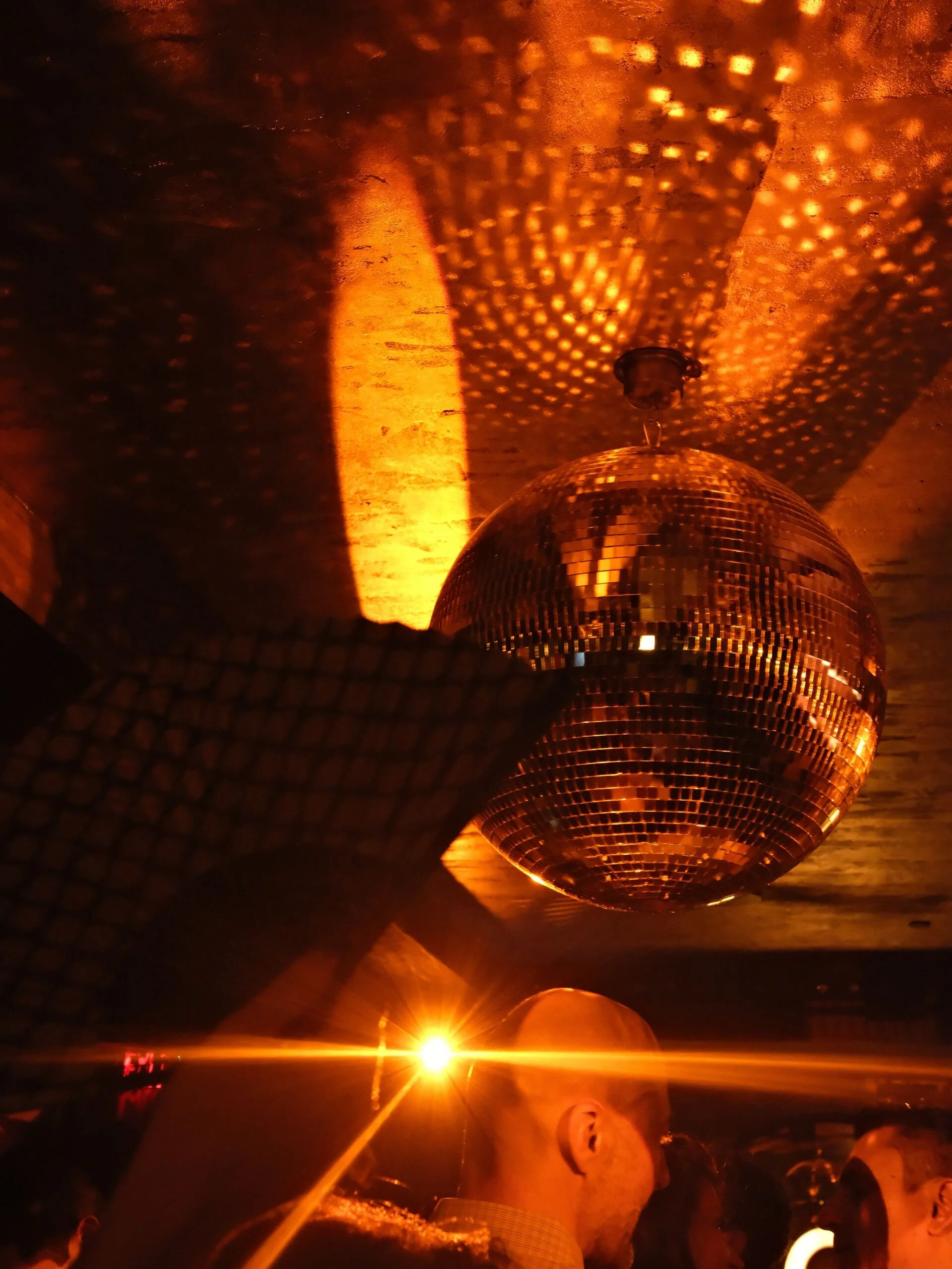 People riding in a vehicle at sunset with a large disco ball hanging from the ceiling, casting patterned reflections on the ceiling and walls.