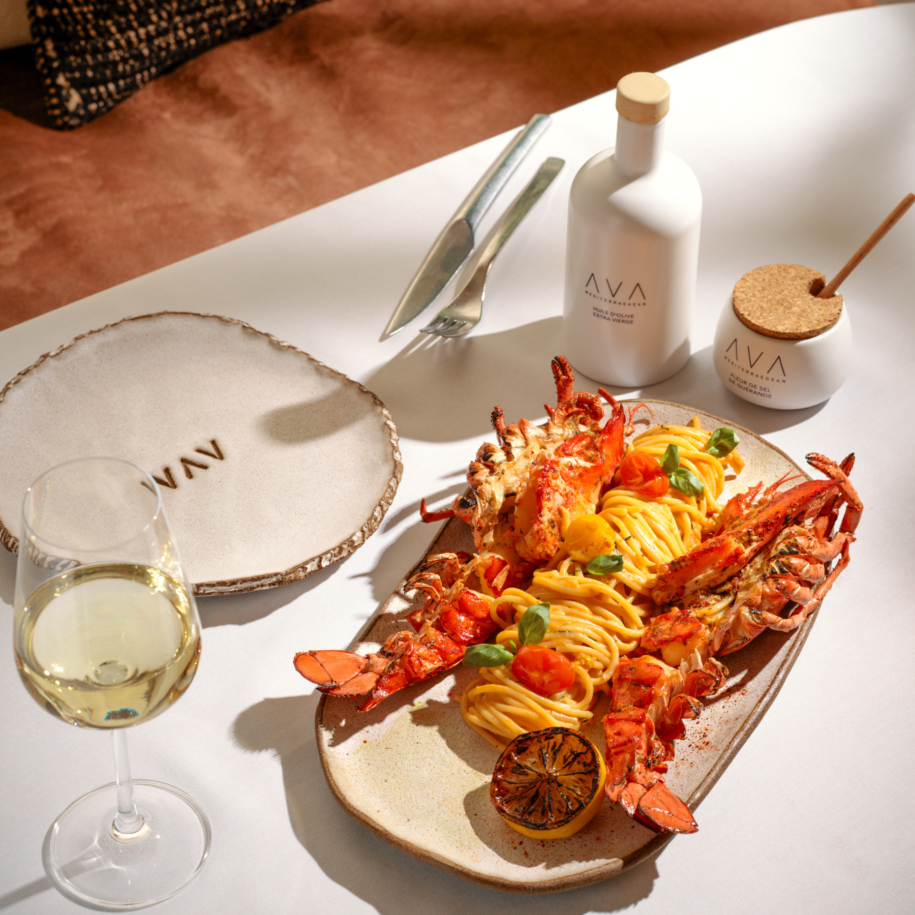 An elegant table setting with a lobster and pasta dish and a wine glass with white wine
