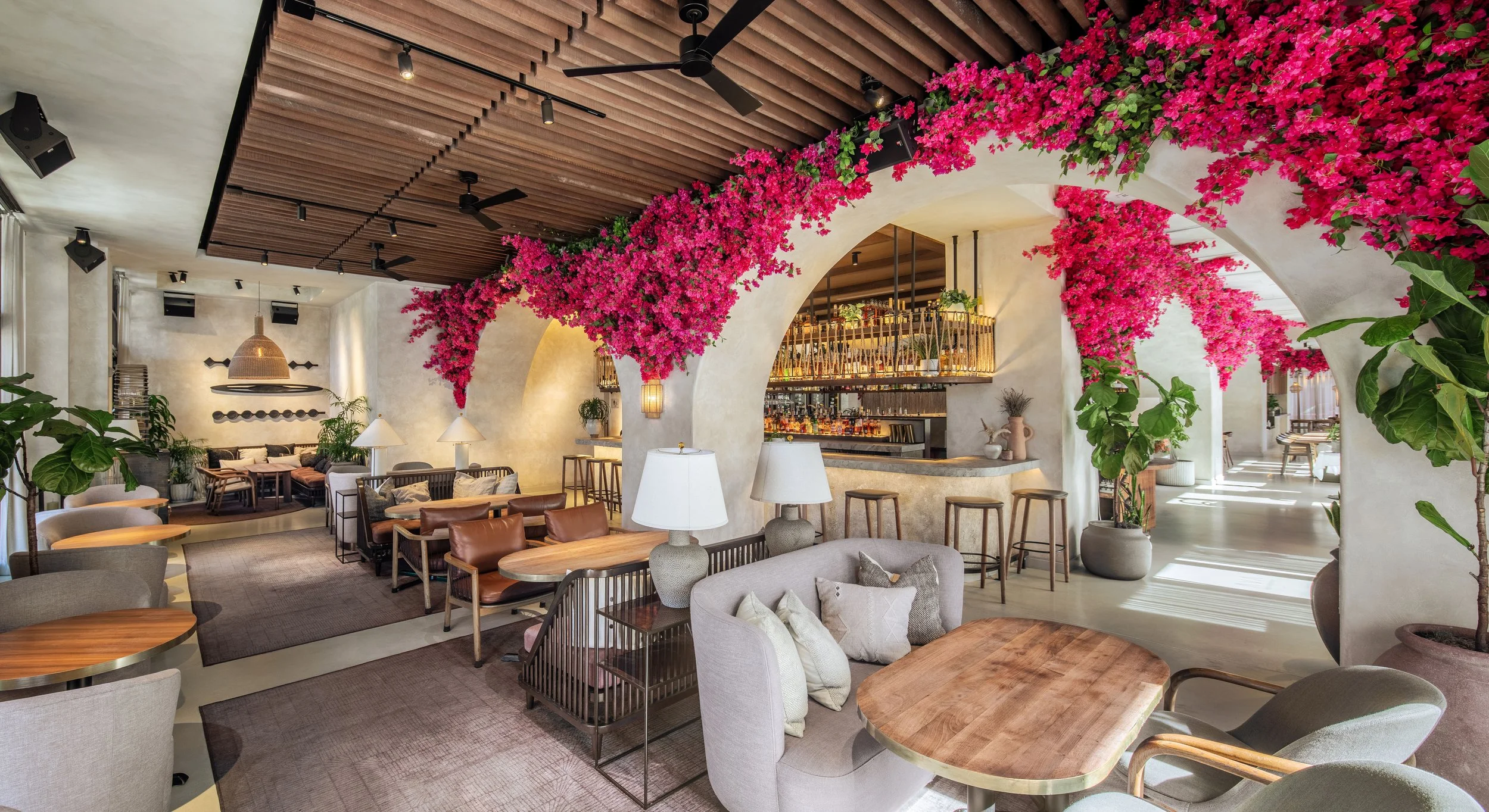 Beautiful dining area of AVA Winter Park, with a bar in the background and pink flowers around the arched walls.
