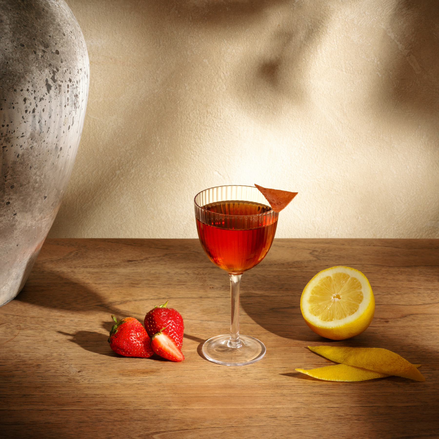 Simple red cocktail on a wooden table with fruit garnishes at AVA MediterrAegean with strawberries and lemon half.