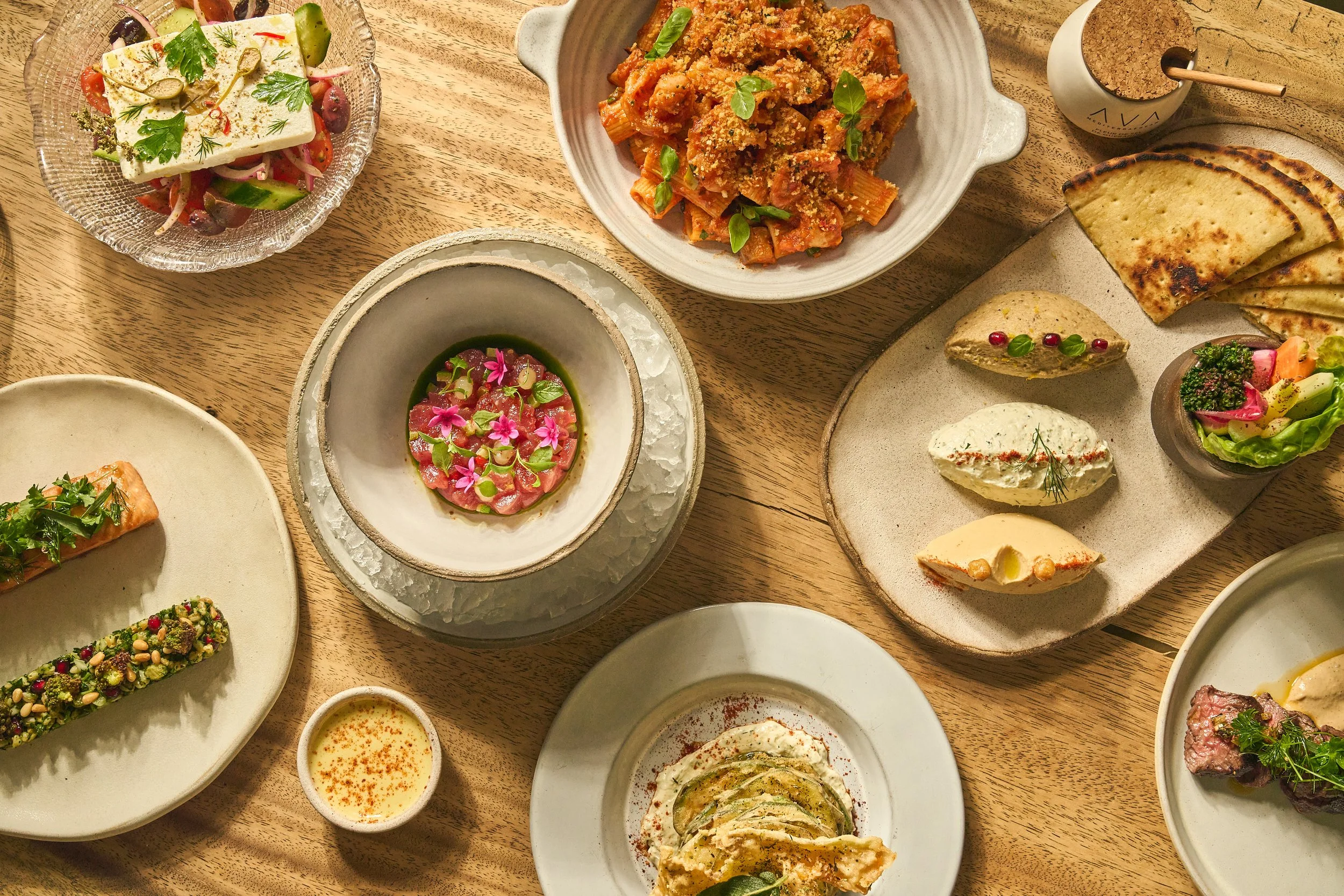 AVA Winter Park's dishes on a table, including a pasta dish, hummus, spreads, and more.