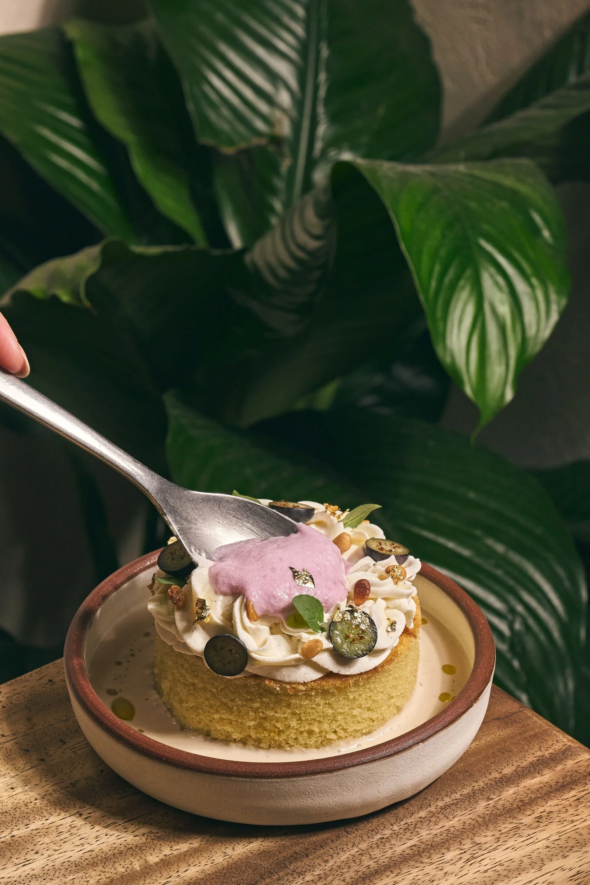 Dessert with cream, berries, edible gold flakes, and a pink fondant decoration, in a bowl on a wooden table.