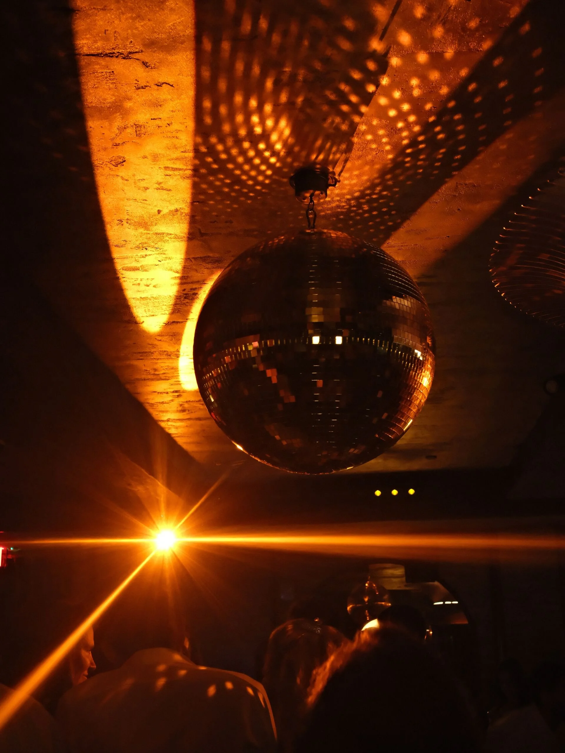 A disco ball hanging from the ceiling projects light patterns onto the walls and ceiling, creating a warm, orange-colored glow in a dimly lit room.