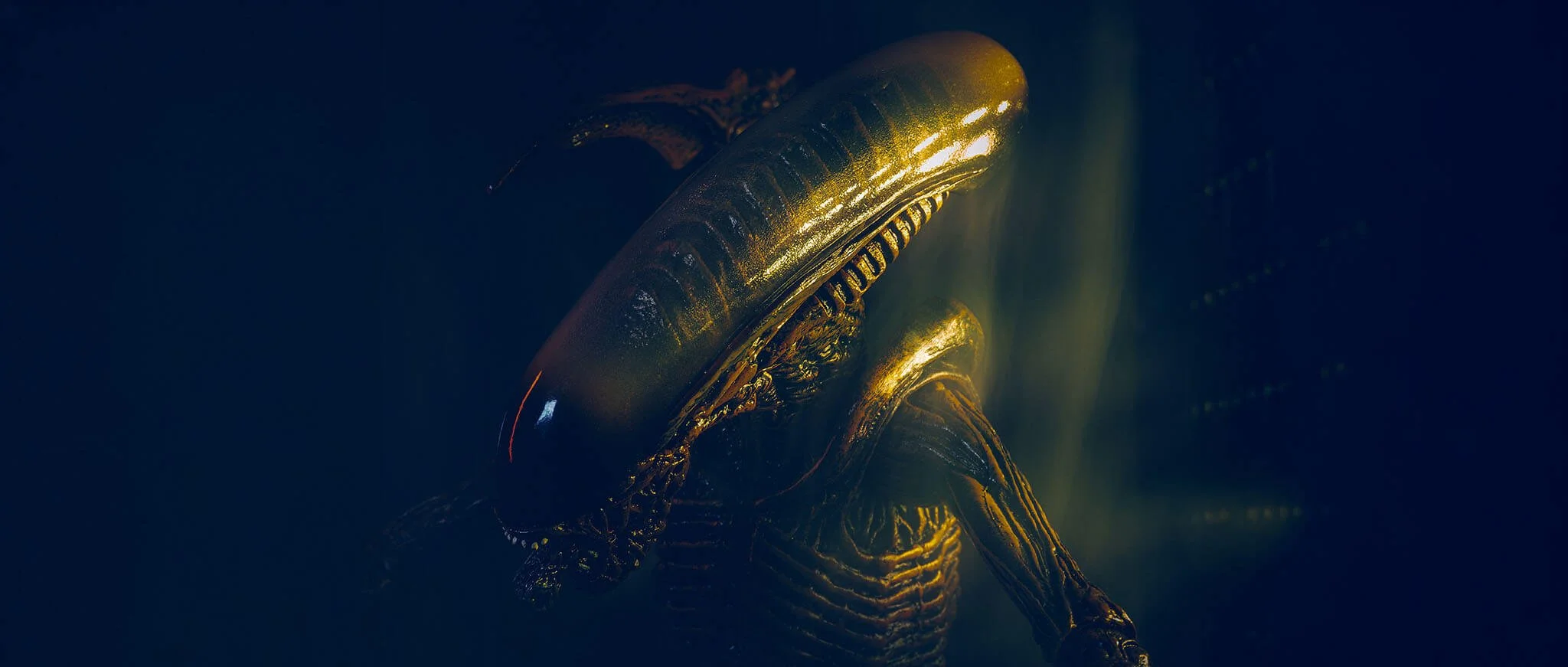 Close-up of a futuristic, metallic, and gold-embellished alien or robot figure in a dark setting with dramatic lighting.