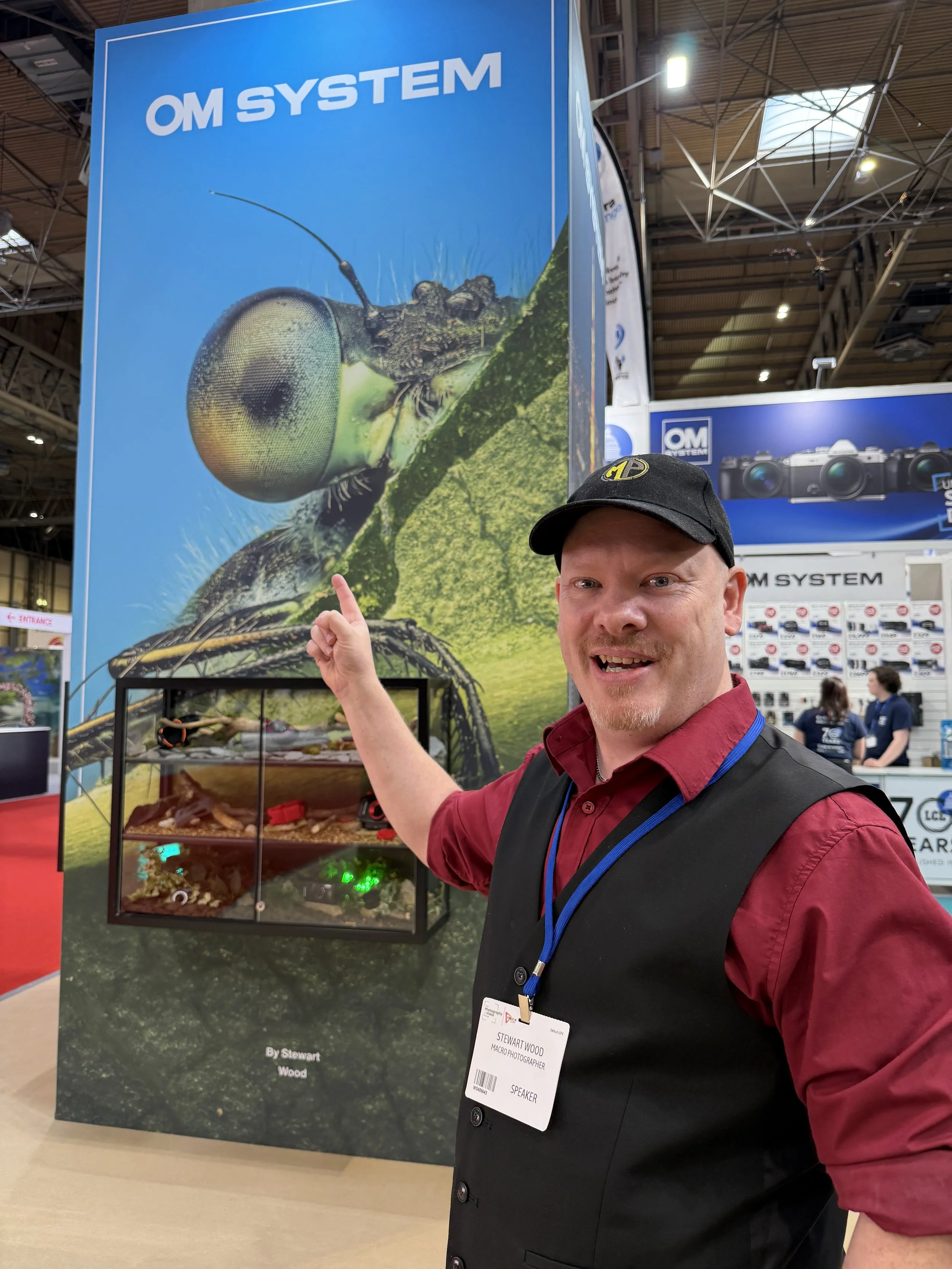 Man pointing at large banner featuring an insect and a bug in a display case at a trade show.
