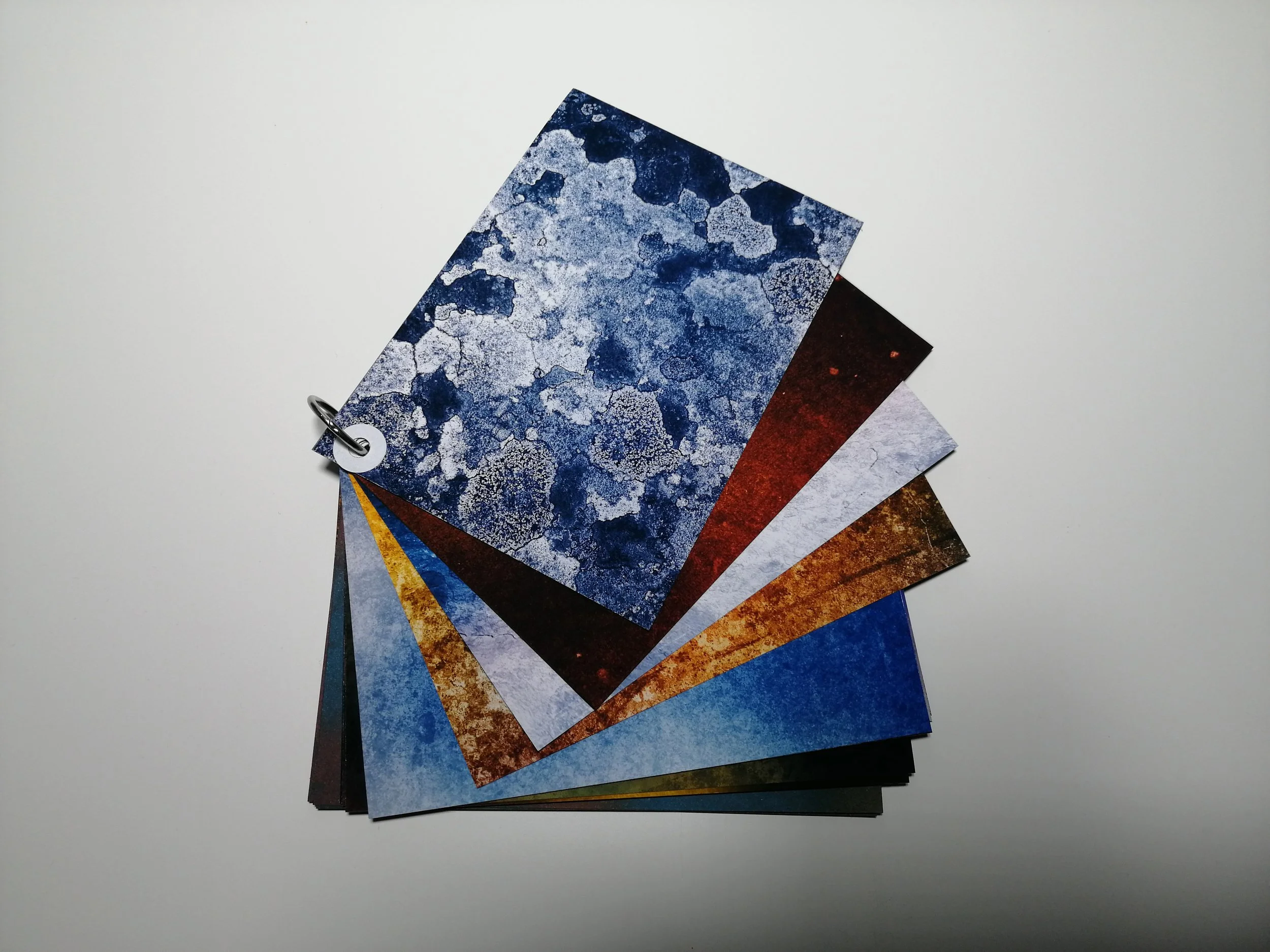 Collection of color sample cards with various abstract patterns in shades of blue, red, yellow, and white, fanned out on a white surface.