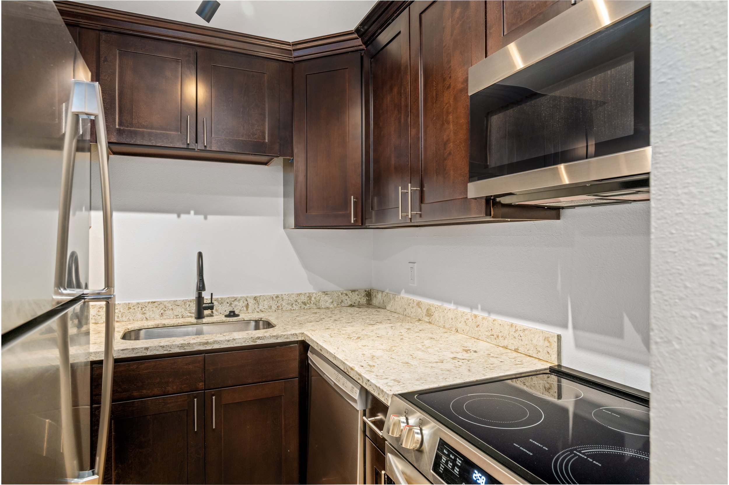 Kitchen with dark wooden cabinets, granite countertop, stainless steel microwave, electric stove, and a small sink with a black faucet.
