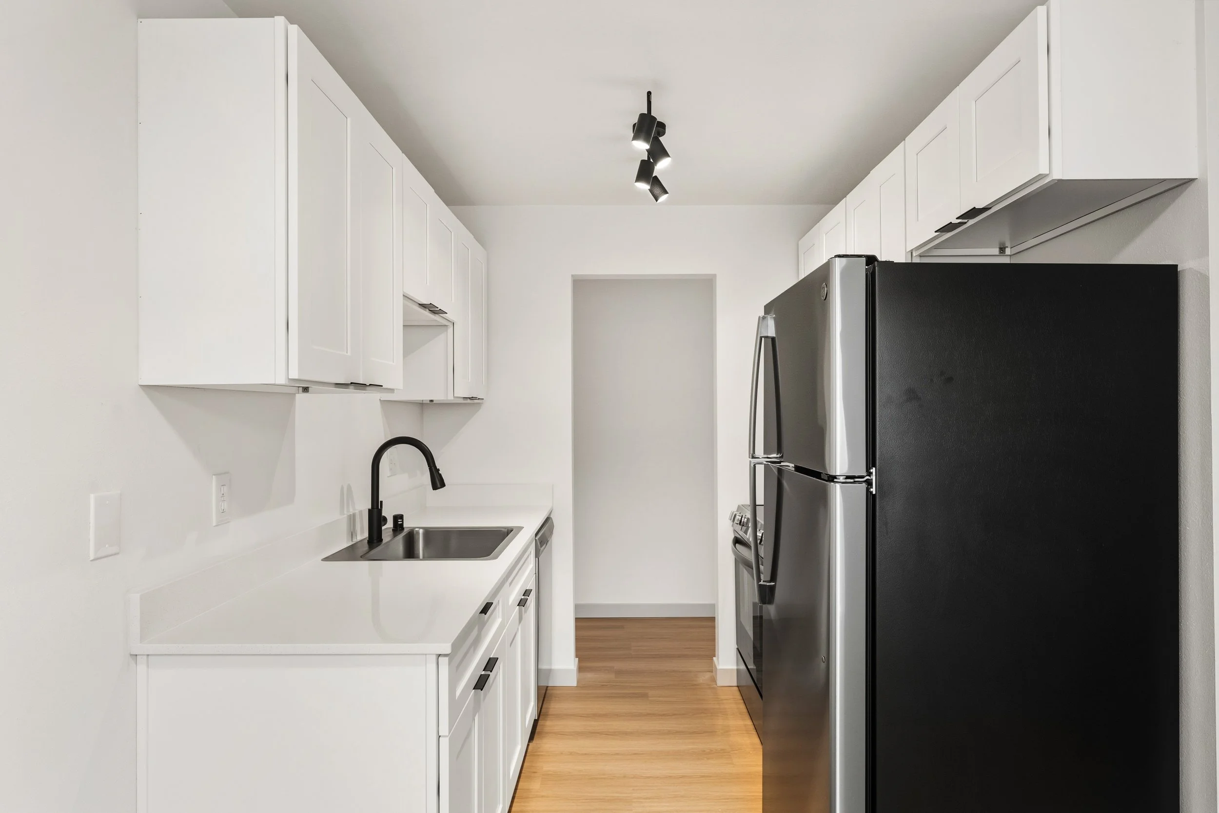 Modern kitchen with white cabinets, black faucet, stainless steel refrigerator, black stove, and wooden floor.