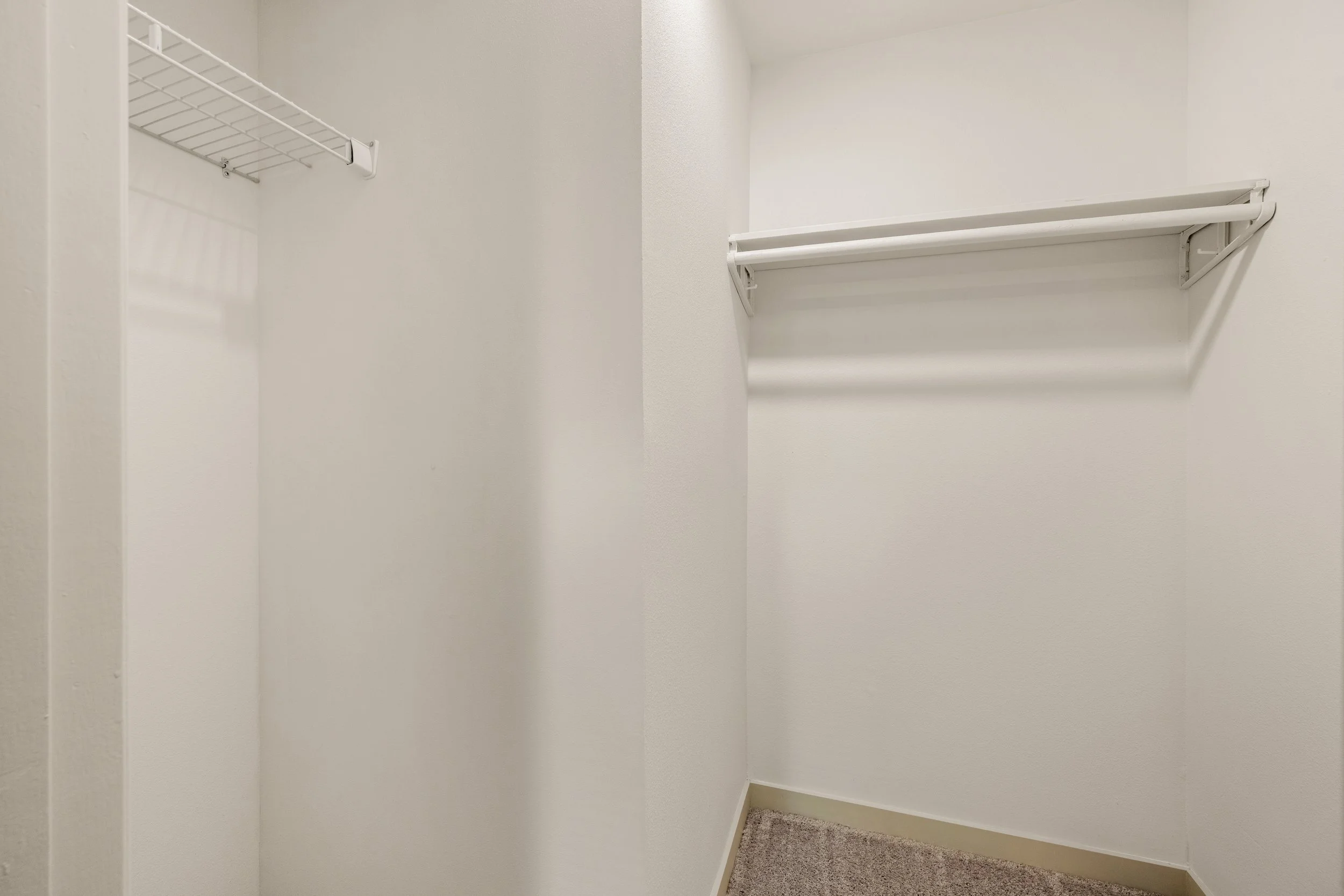 Empty walk-in closet with white wire shelving on white walls and carpeted floor.