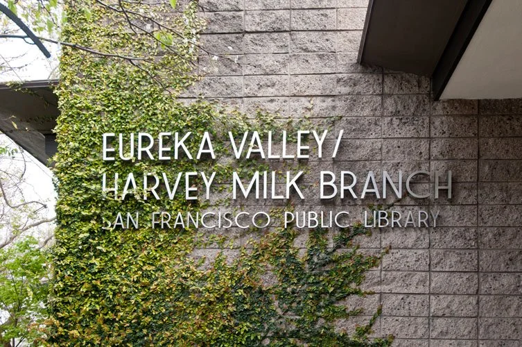 Sign for Eureka Valley/Harvey Milk Branch, San Francisco Public Library, mounted on a brick wall partially covered with green ivy.