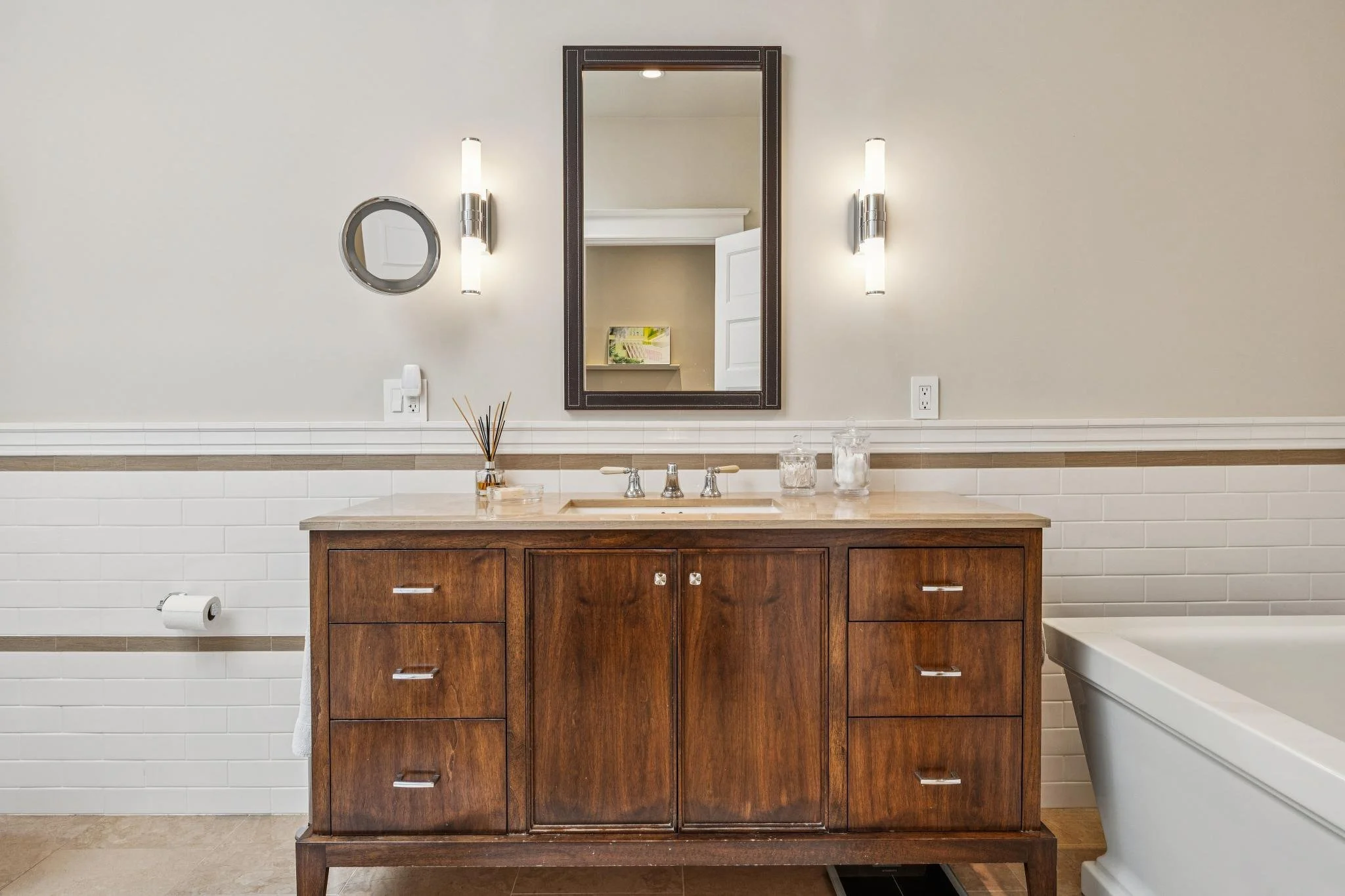 Bathroom vanity with a wooden cabinet, marble countertop, mirror, and wall-mounted lights.