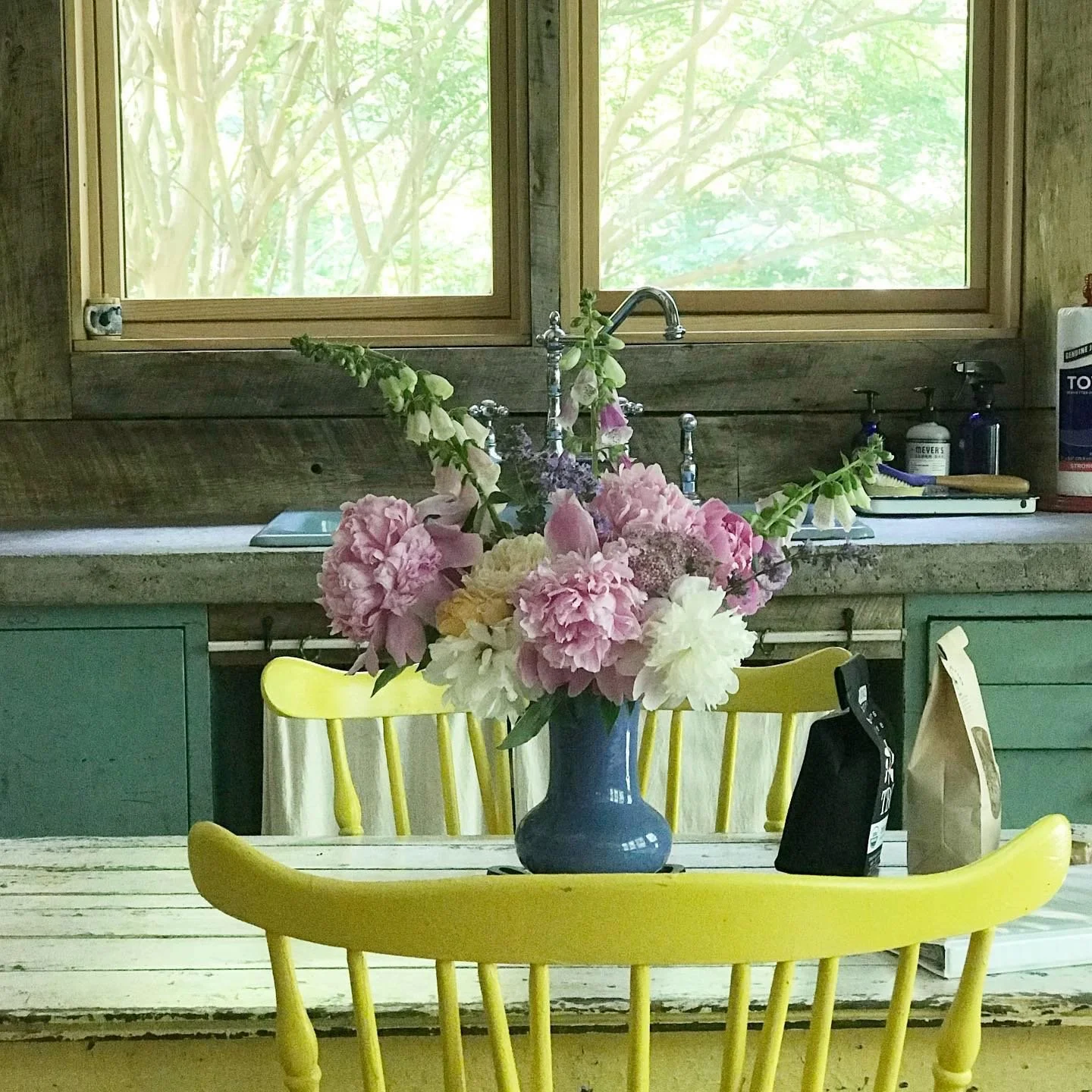 A bouquet of pink, white, and purple flowers in a blue vase on a wooden dining table with yellow chairs