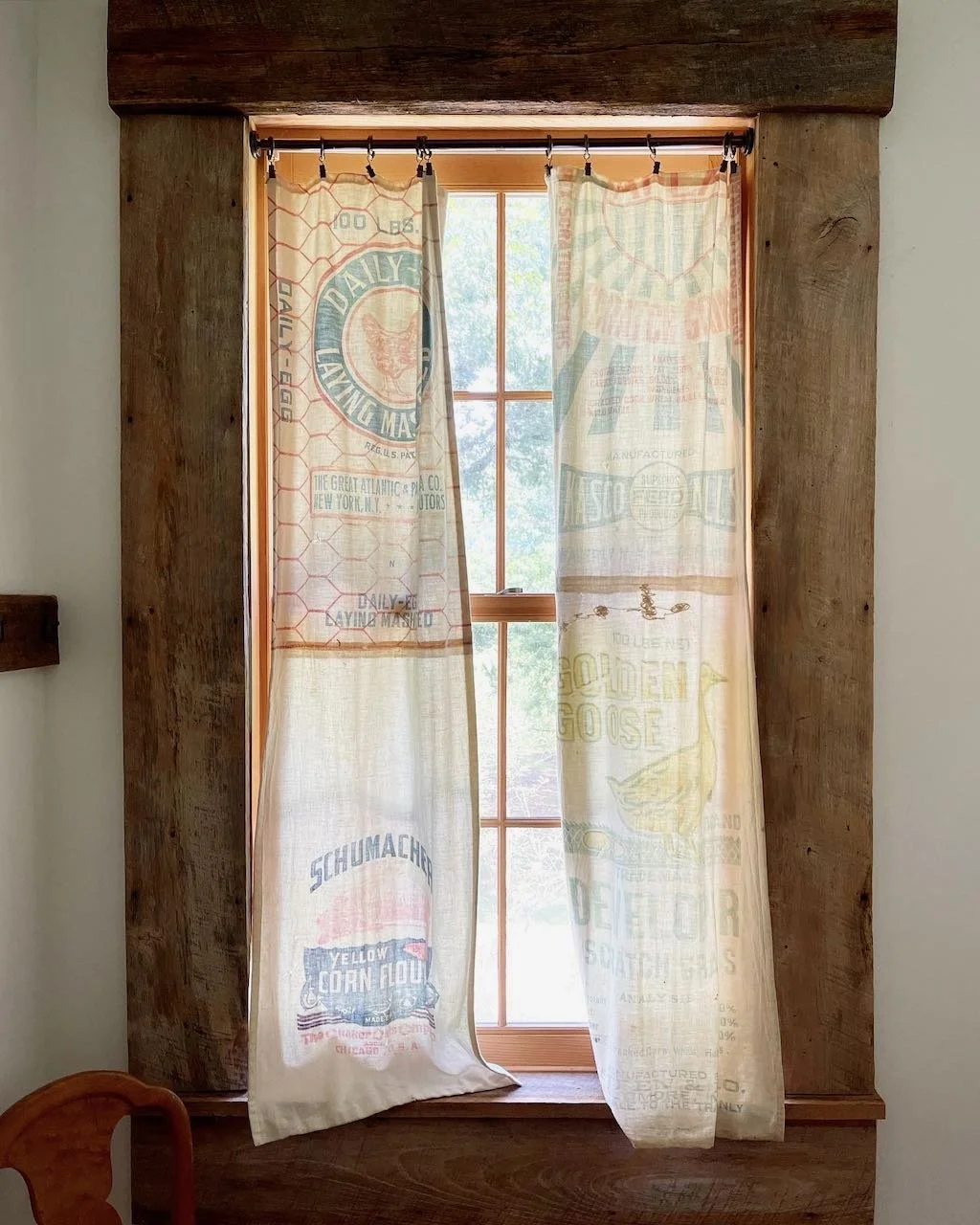 A window with vintage print curtains in a rustic wooden frame, allowing natural light to brighten a cozy interior.