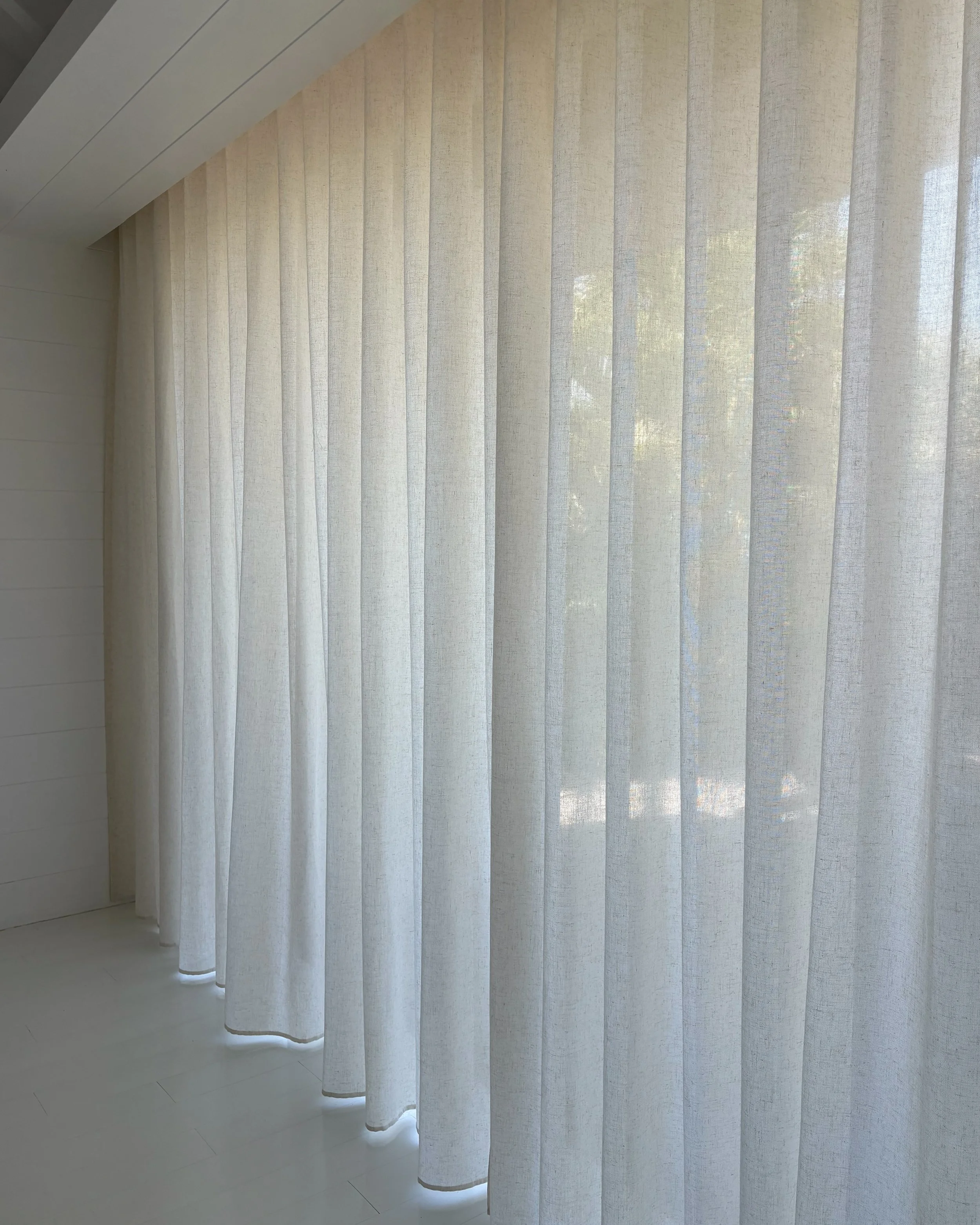 Light-colored vertical blinds covering a large window, with sunlight filtering through.