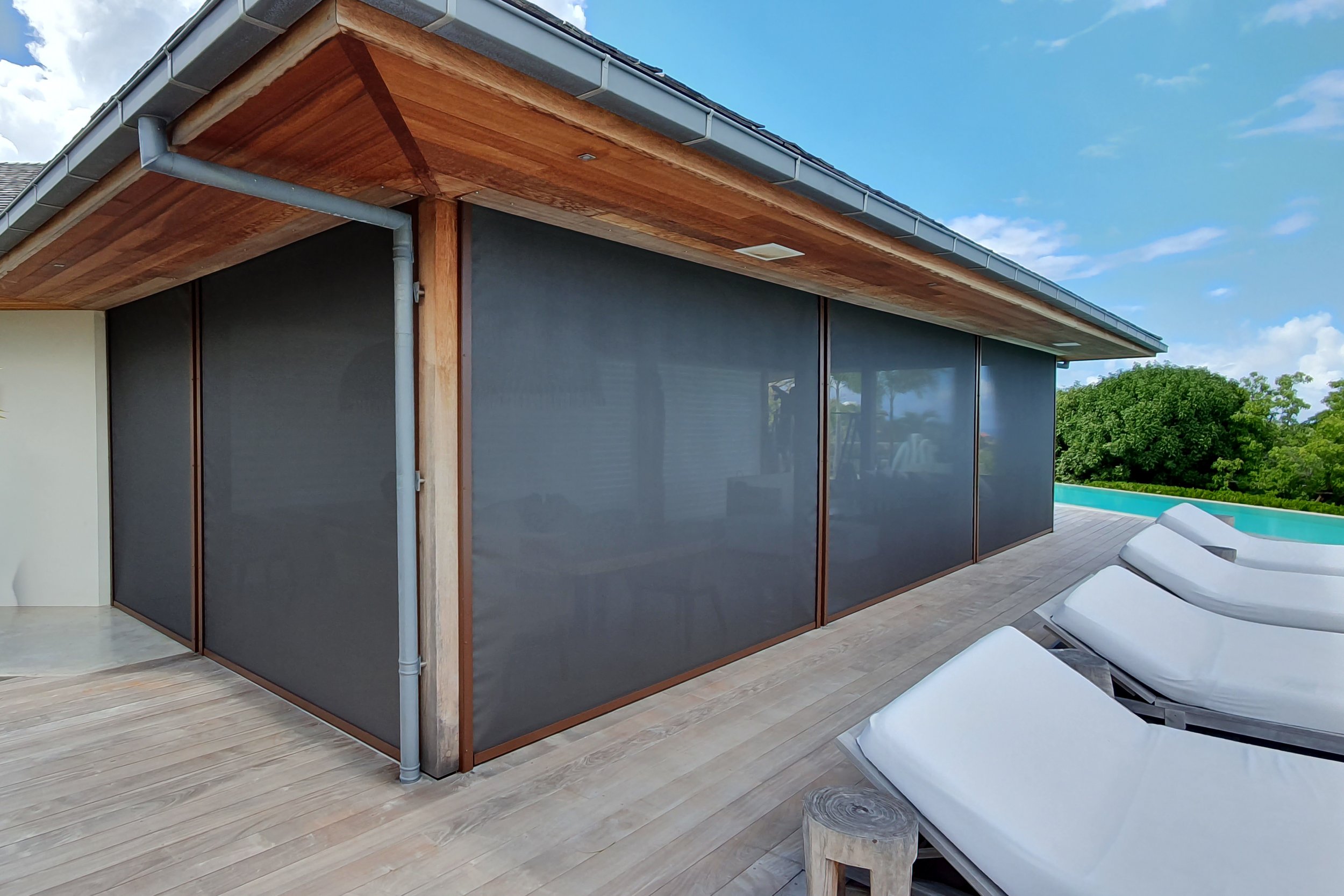 Modern house exterior with wooden overhang, gray walls, and outdoor lounge chairs beside a swimming pool.