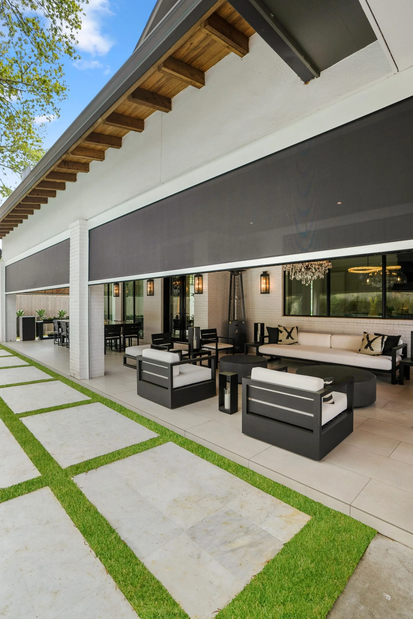 Modern outdoor patio and seating area with black and white furniture, large windows, chandelier, and a patio with grass-lined concrete tiles.