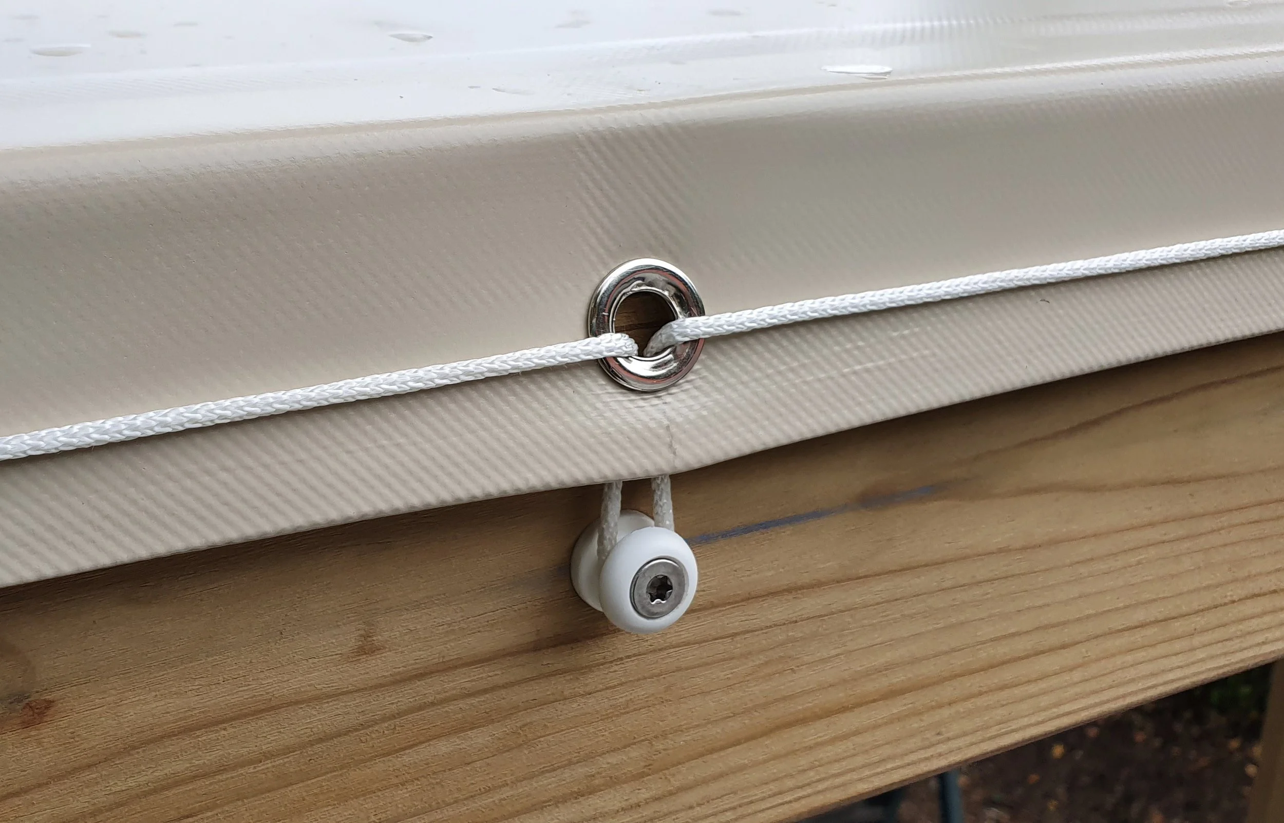 Close-up of a awning with a metal eyelet and a white drawstring, covering a wooden roof structure.