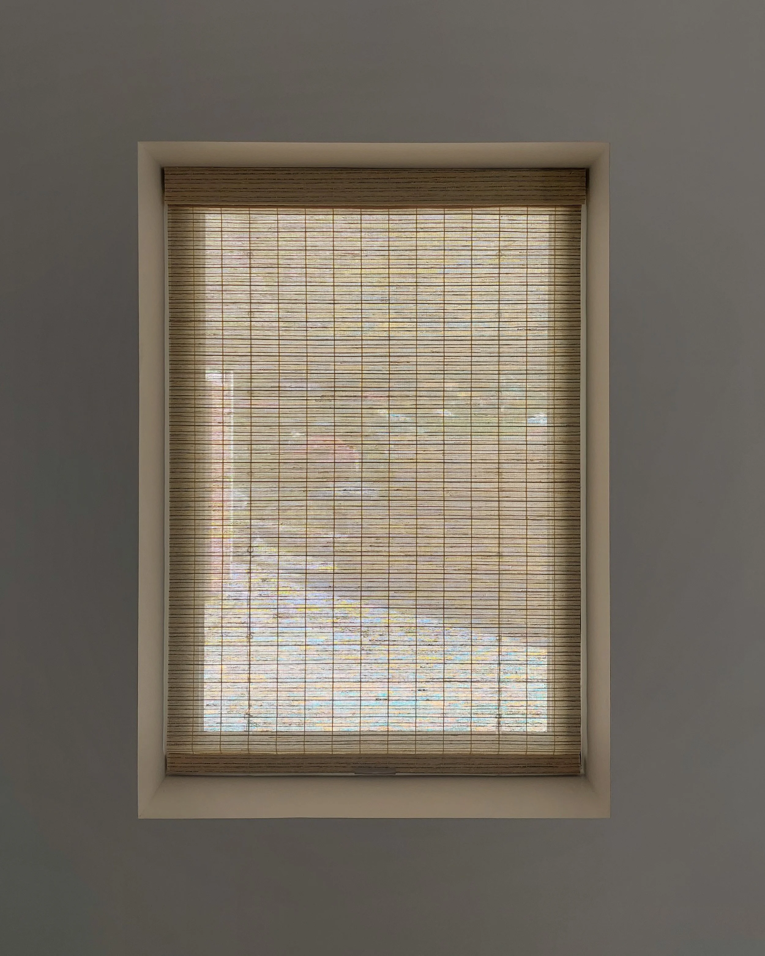 View of a rectangular window with a bamboo blind, seen from inside a room with white walls, looking up at the ceiling.