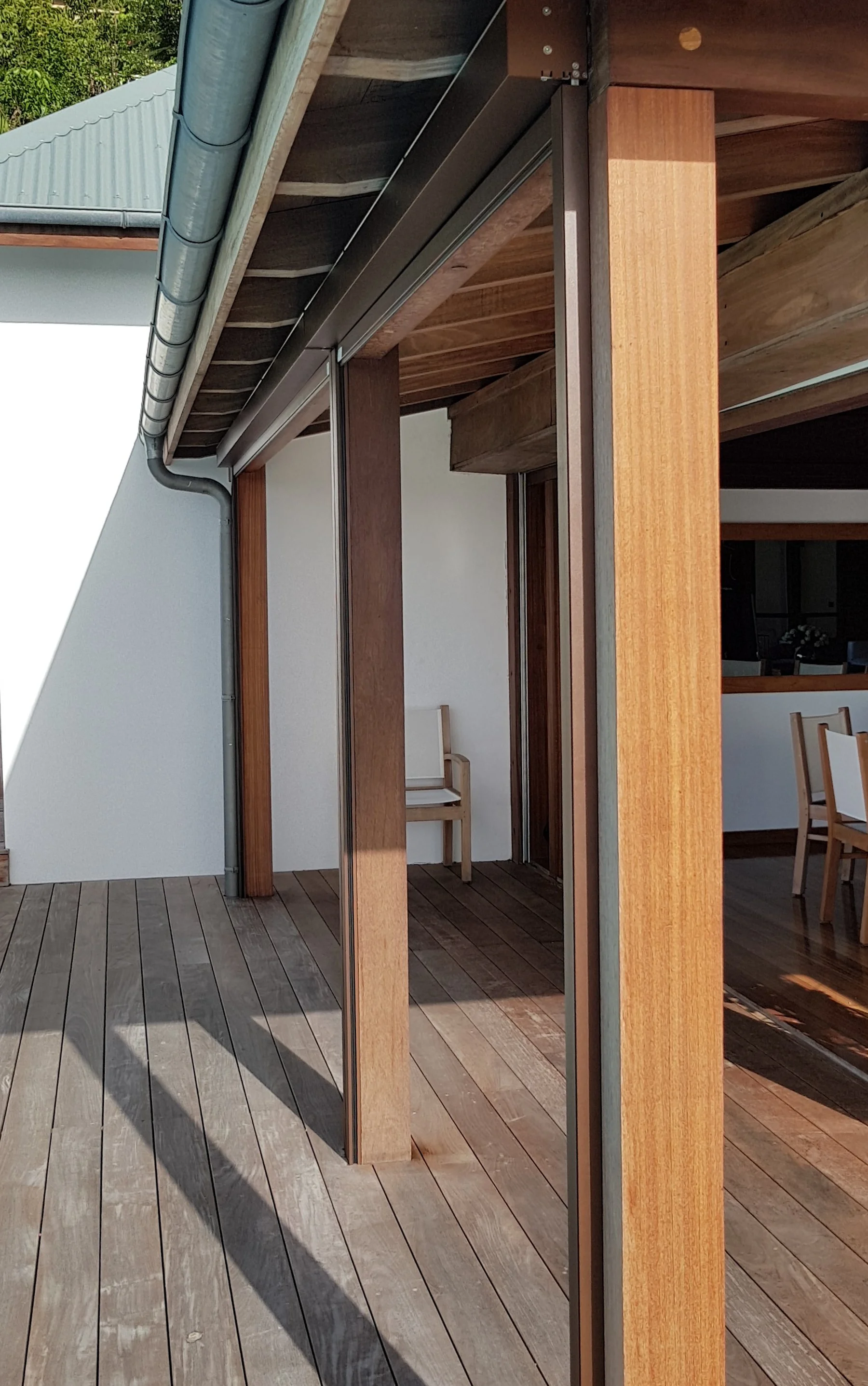 Outdoor patio with wooden flooring and modern design, featuring wooden posts, glass walls, and a rain gutter on the roof.