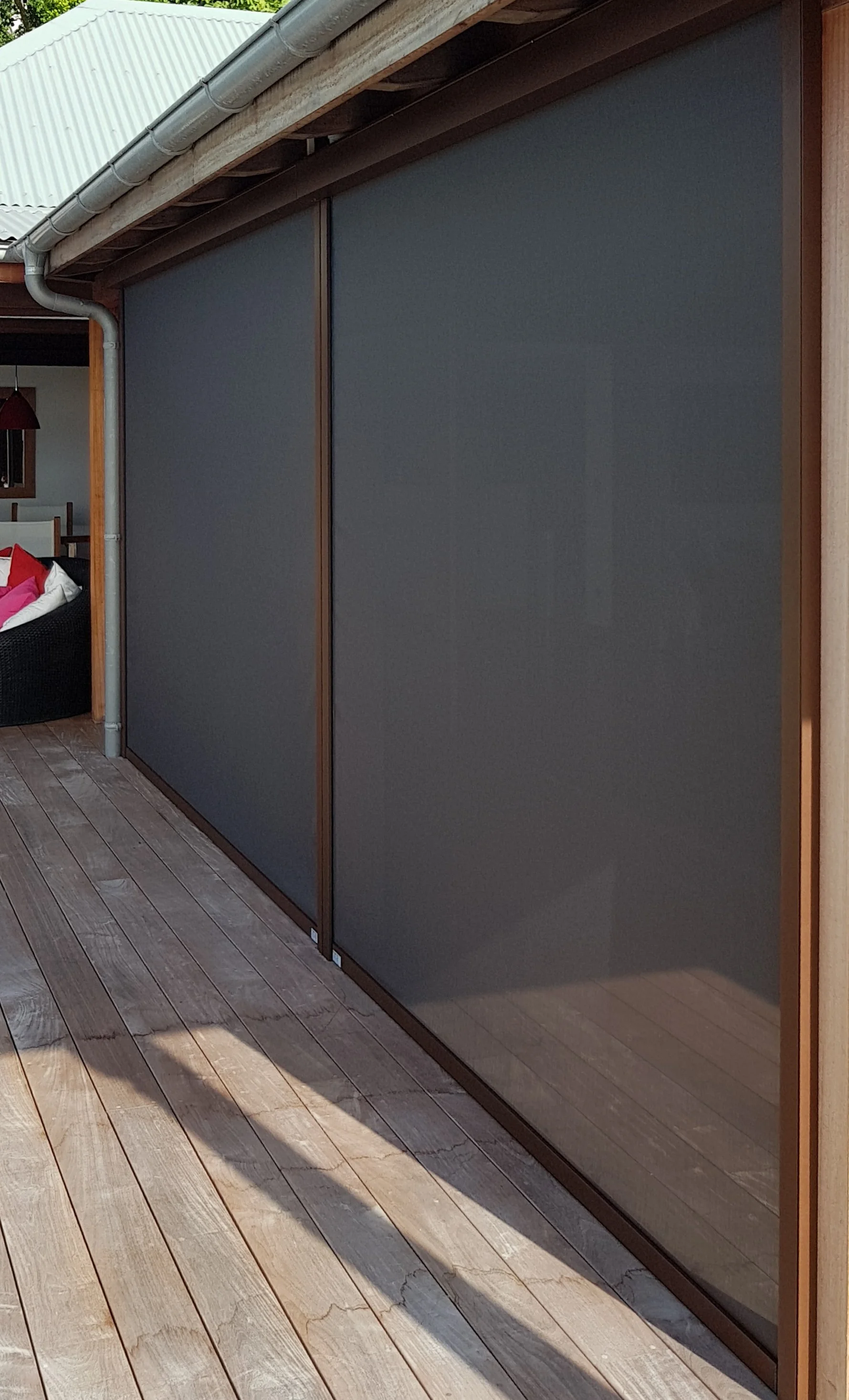 A large gray sliding door with a wooden frame, adjacent to a section of wooden flooring, on an outdoor deck or patio area.