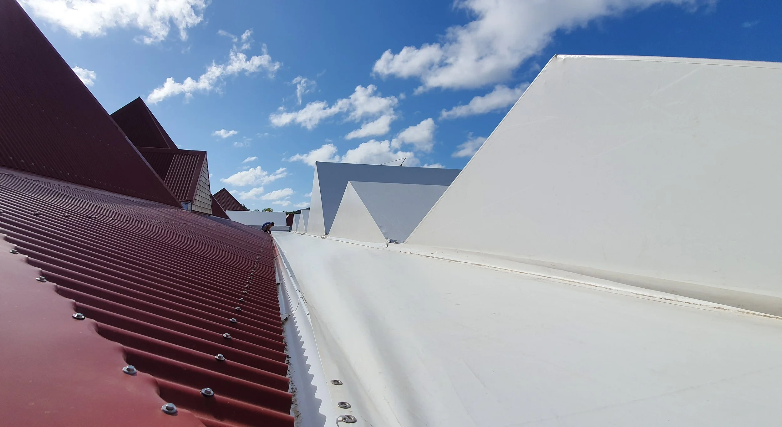 Roof with red corrugated metal sheets and white panels under a blue sky with scattered clouds.