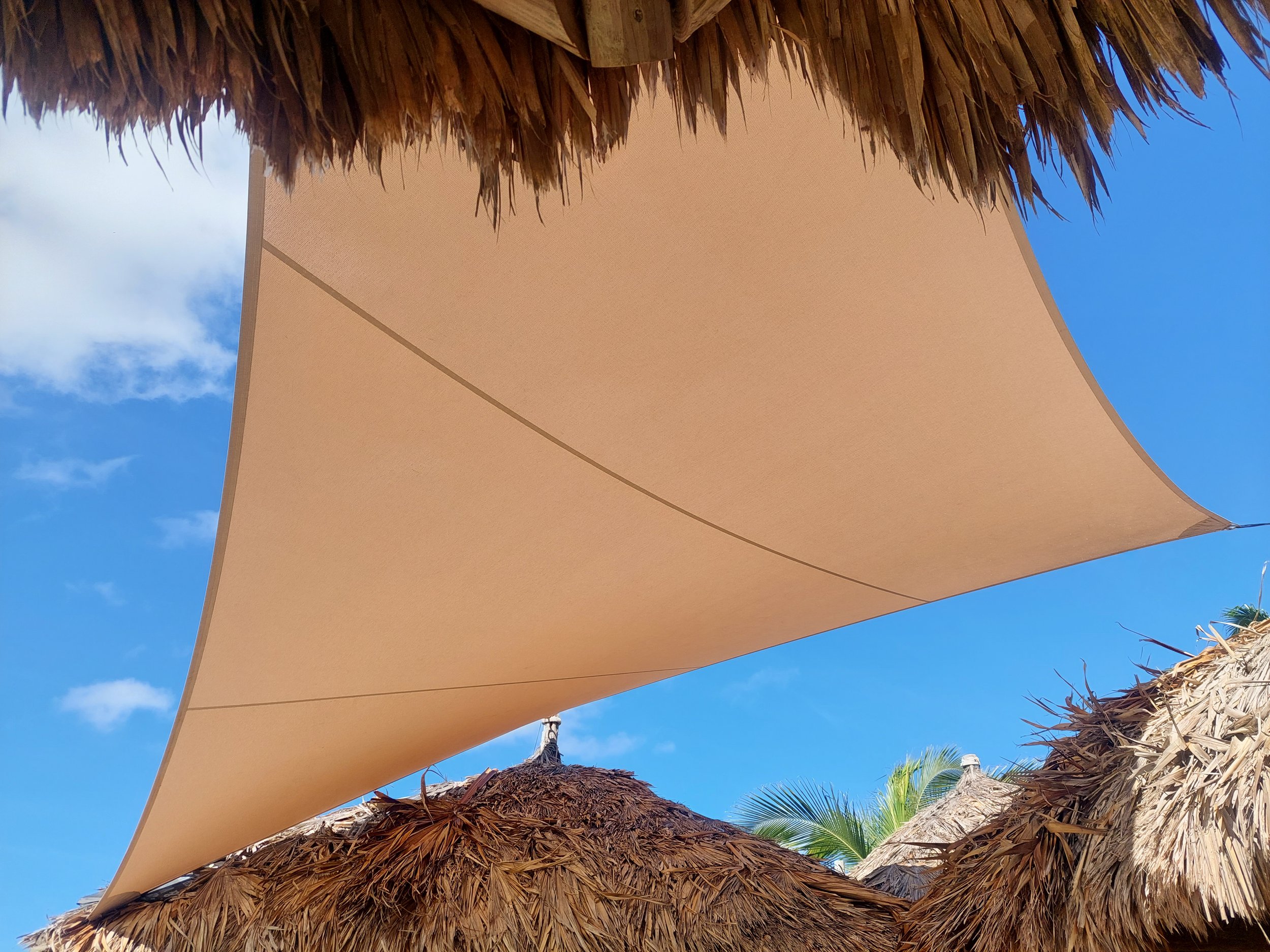 Part of a beige sunshade or umbrella with a thatched roof and blue sky in the background.