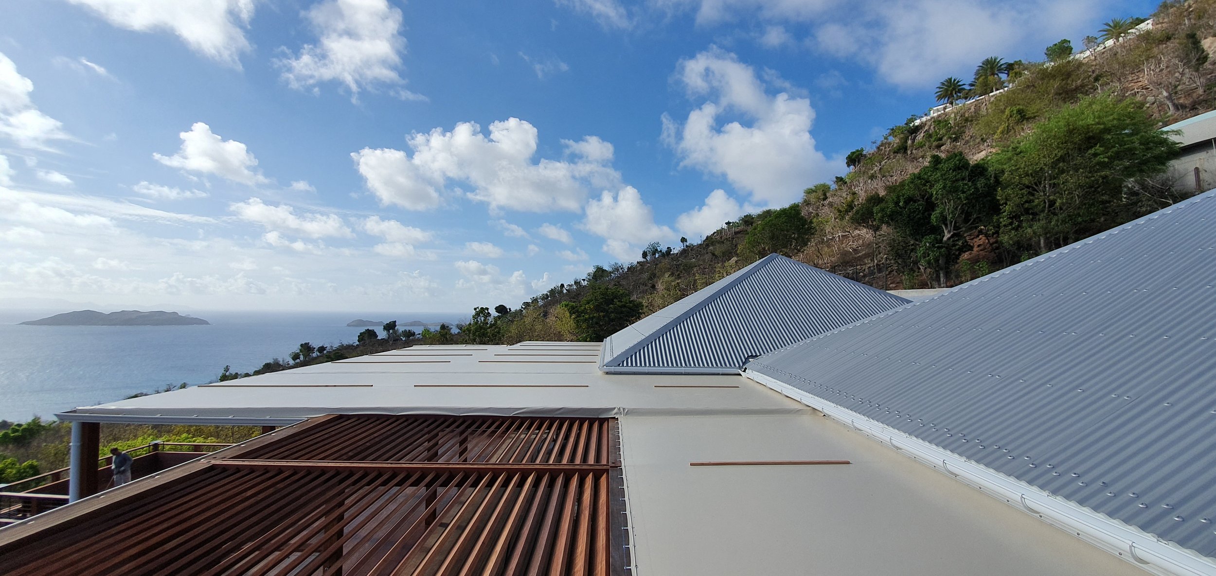 Building with a awning on a hill overlooking the ocean and distant islands, with trees and a partly cloudy sky.
