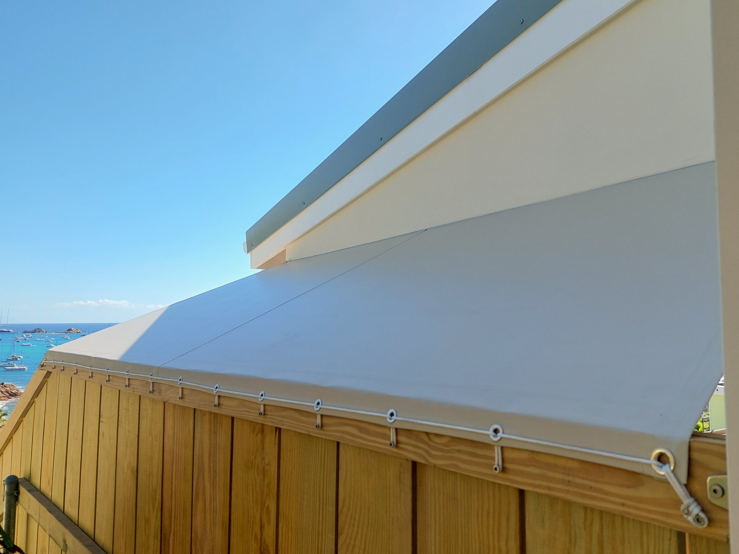 Close-up of a building with a modern, minimalist architectural design featuring a white overhang and a wooden lower section, with a blue sky and ocean in the background.