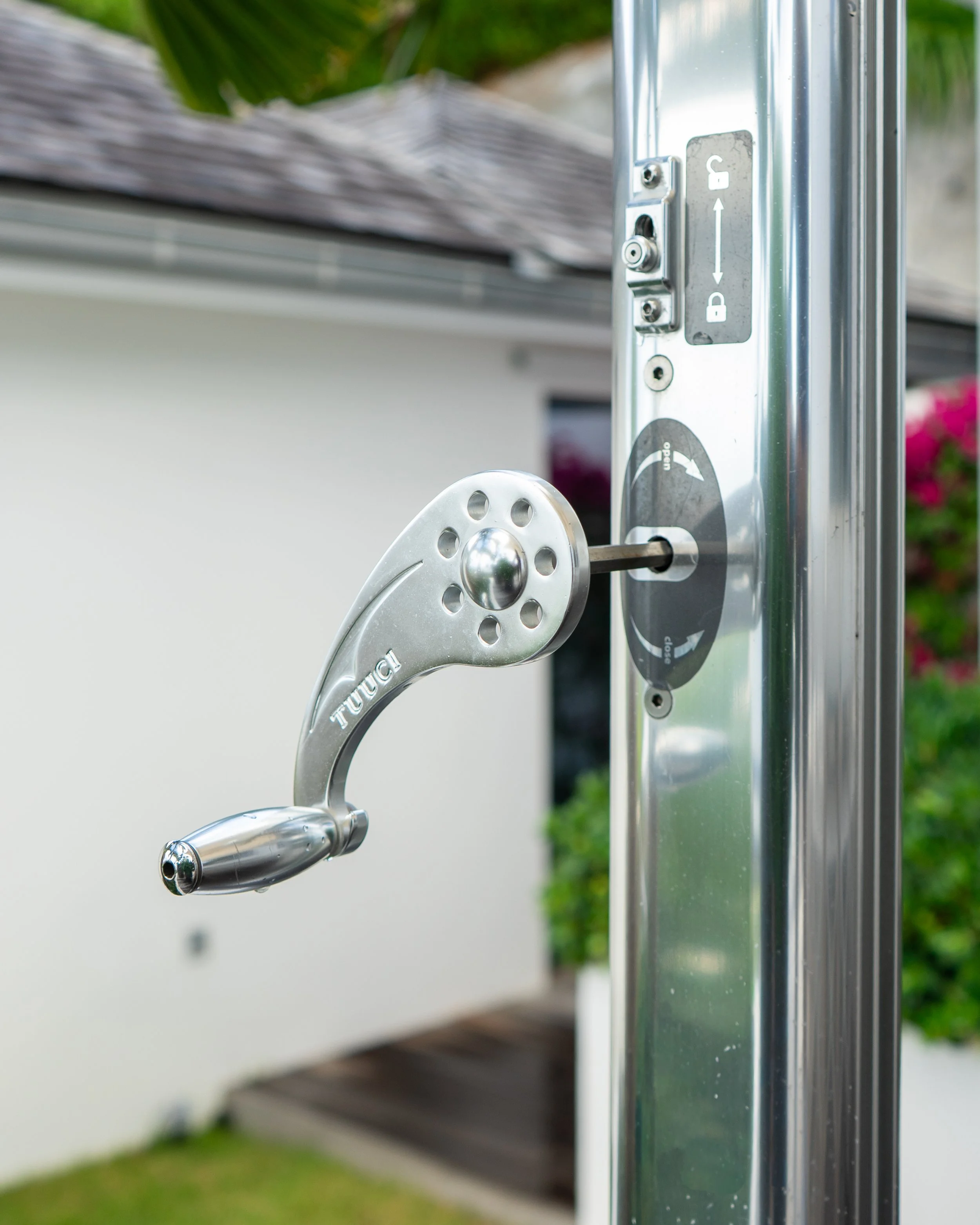 Close-up of an outdoor push button door release with a metallic handle on a stainless steel post, in a green outdoor setting.