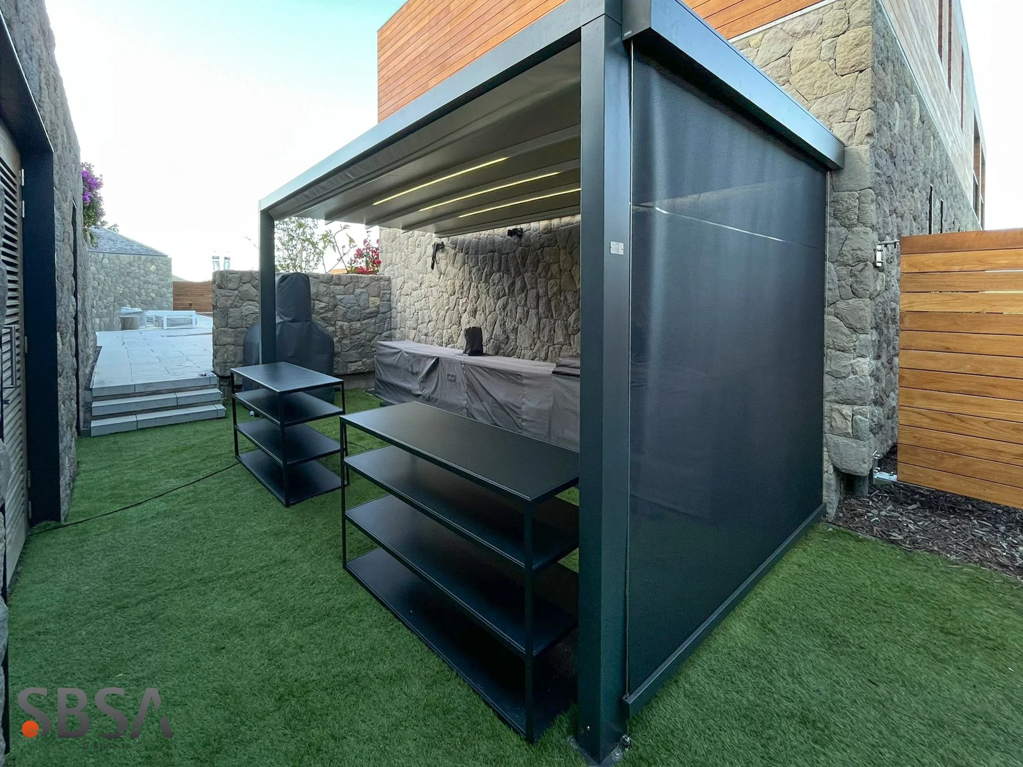 Modern retractable pergola with integrated side screens installed in a contemporary outdoor living space. Featuring a sleek black aluminum structure, ambient LED lighting, and weather-resistant fabric screens.