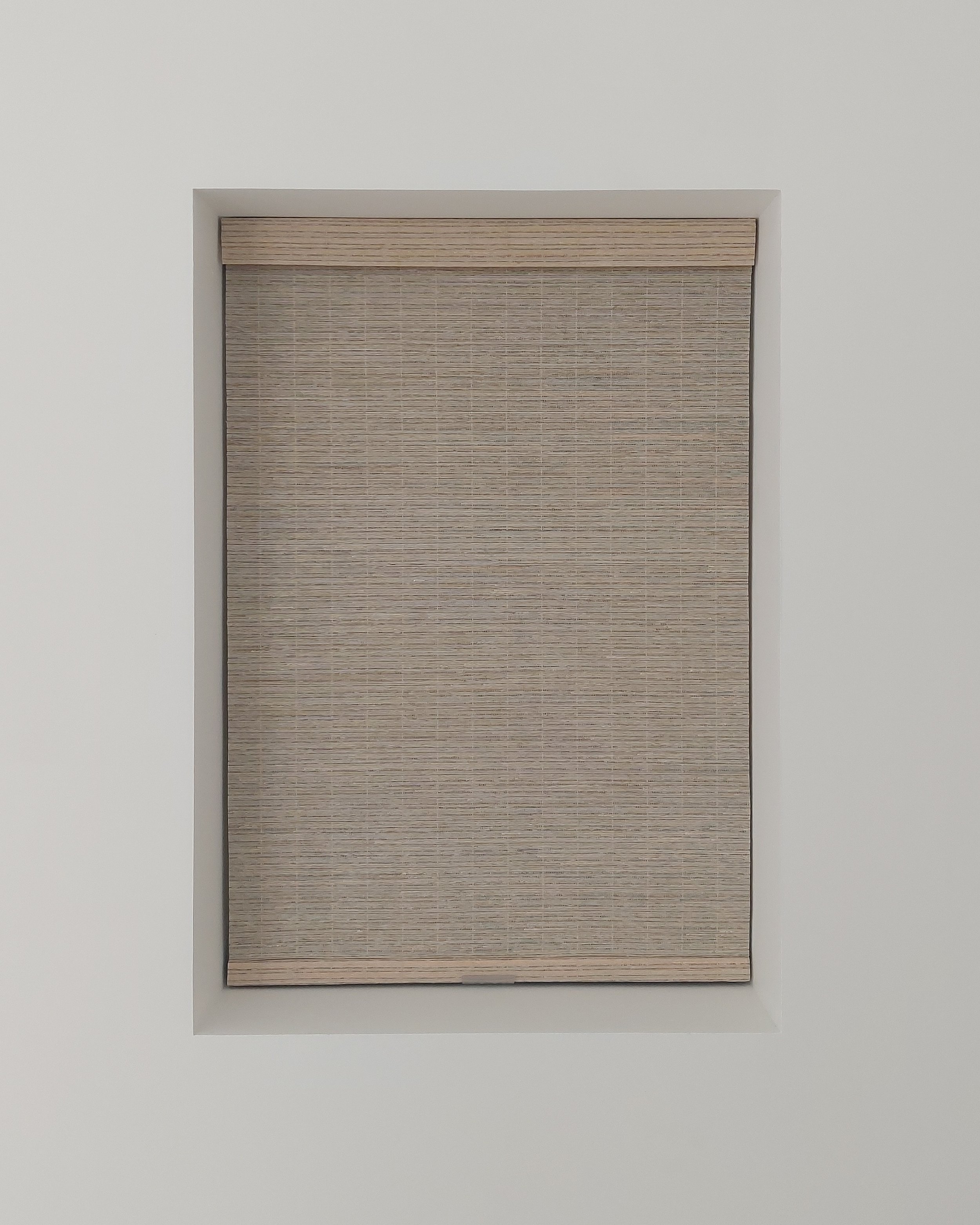 Back of a window-mounted beige pleated shade on a white wall.